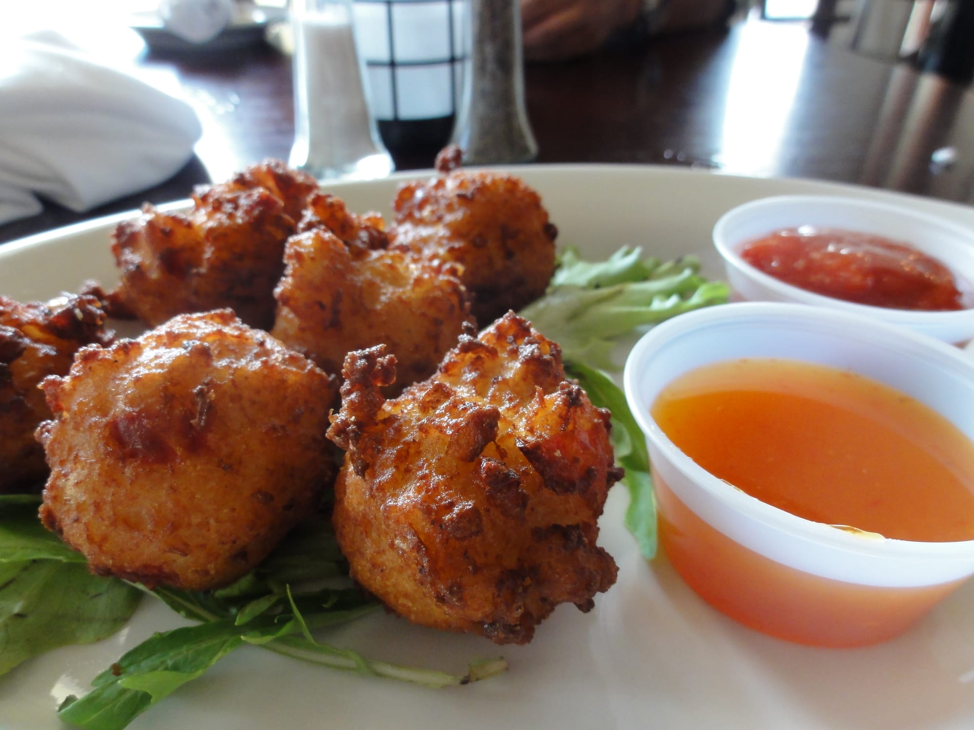 A plate of round, deep-golden conch fritters on salad leaves with two small pots of red and orange dipping sauce