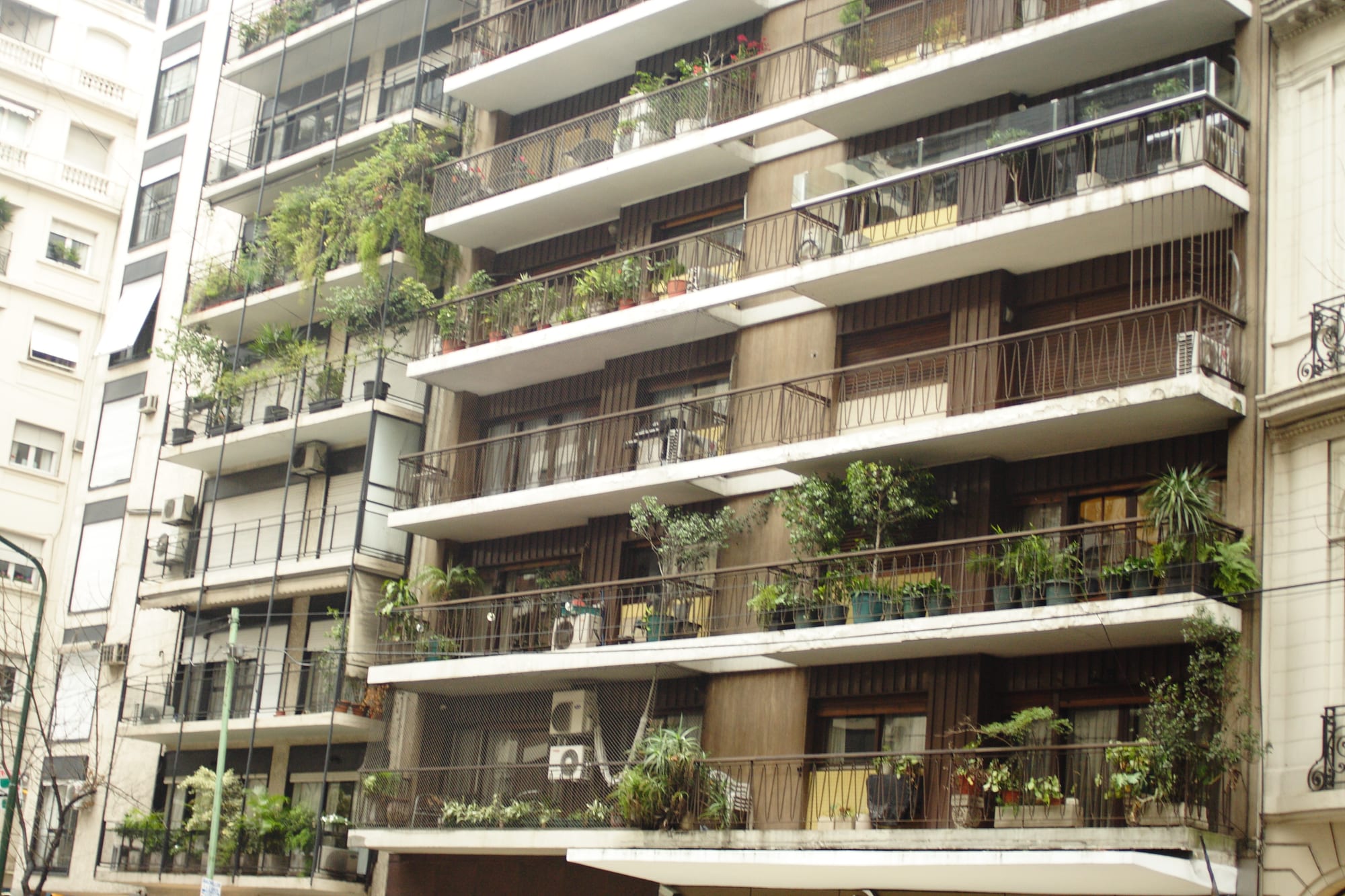 The plant-covered balconies of a tall Buenos Aires apartment block, stacked floor after floor, with older buildings visible alongside