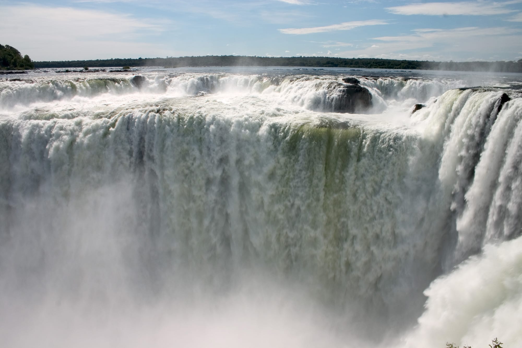A vast semicircle of waterfalls pouring into a canyon wrapped in spray and rainbows