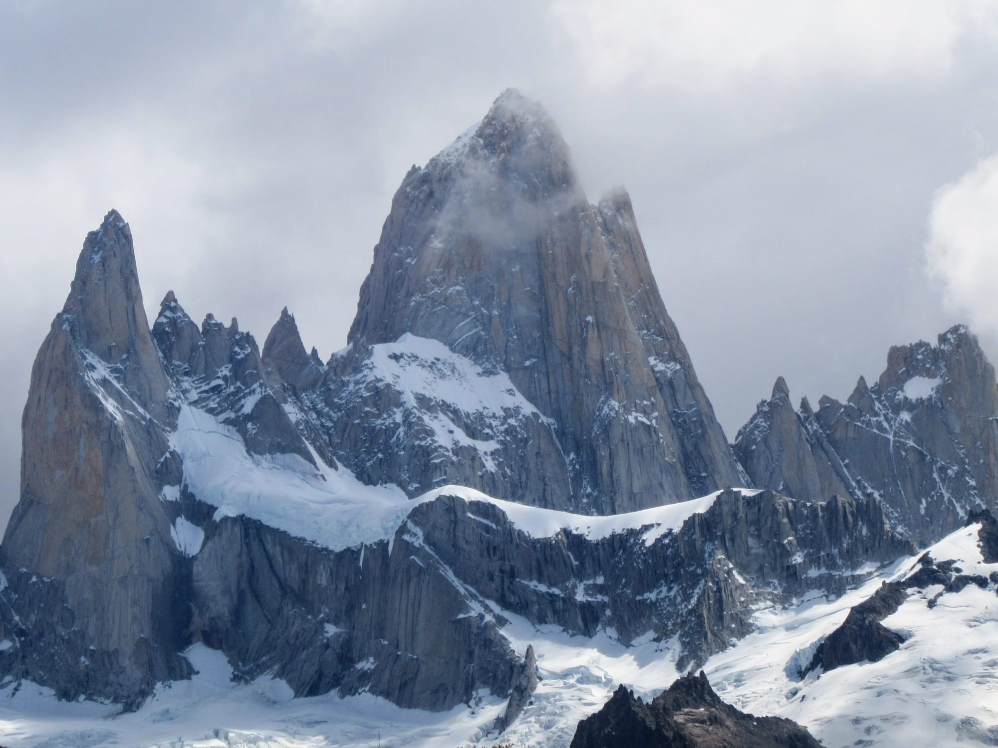 A jagged granite spire and its neighbouring towers rising above a brown ridge, clear sky
