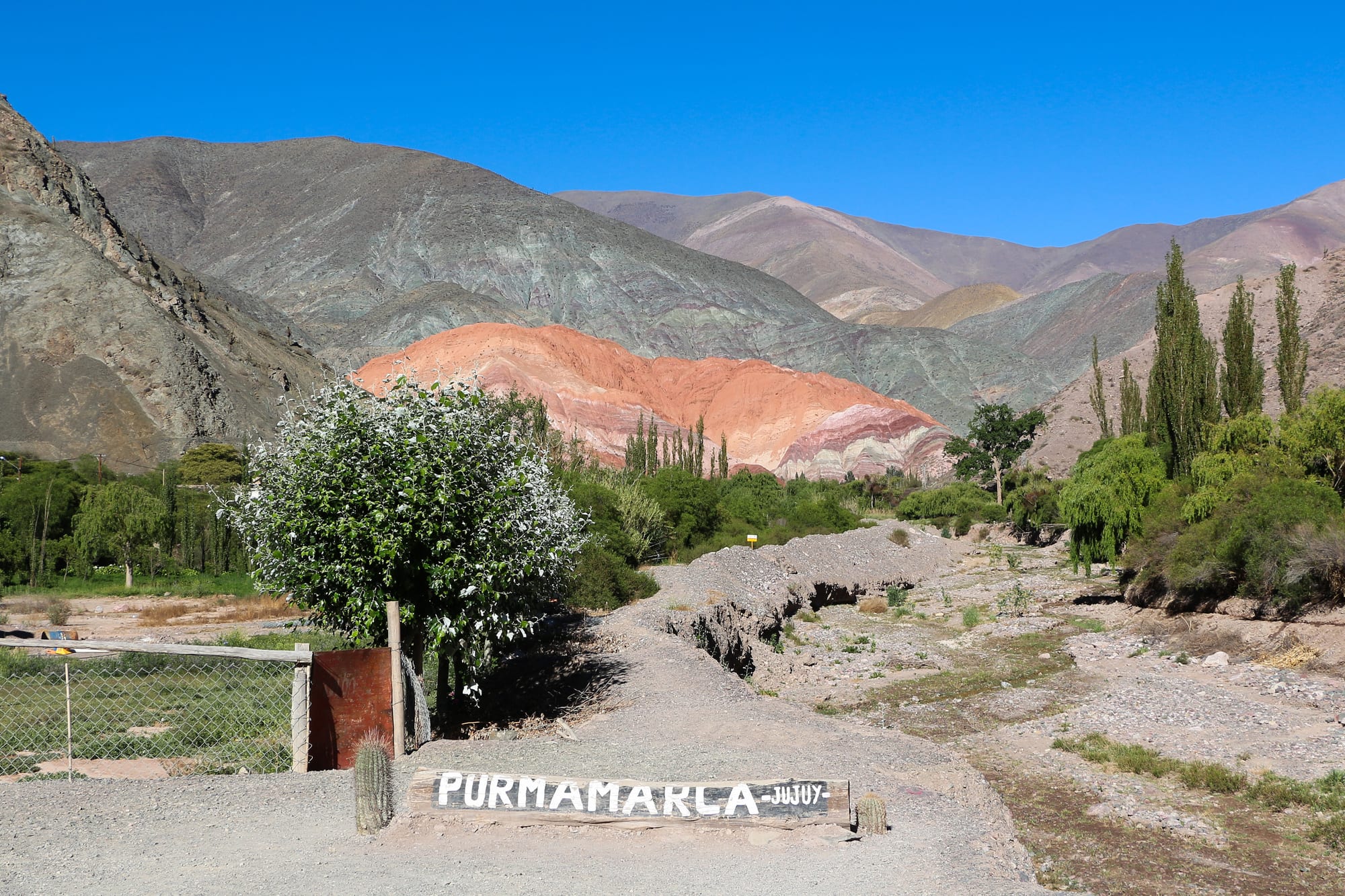 A hillside striped in bands of red, orange, green and purple rock above an adobe village