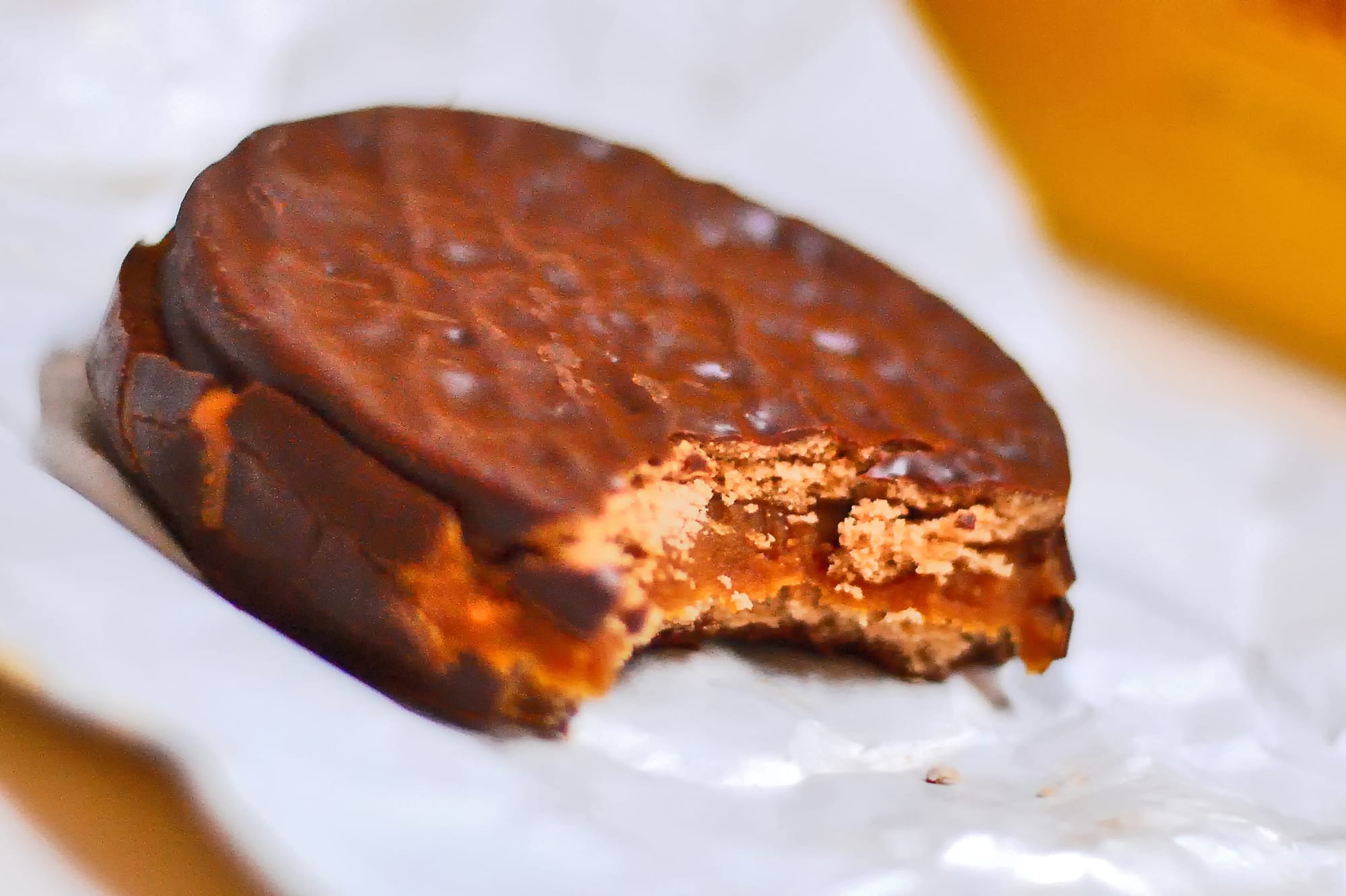 A round chocolate-coated biscuit sandwich with a bite taken out, showing a thick layer of caramel-coloured dulce de leche between two biscuit layers