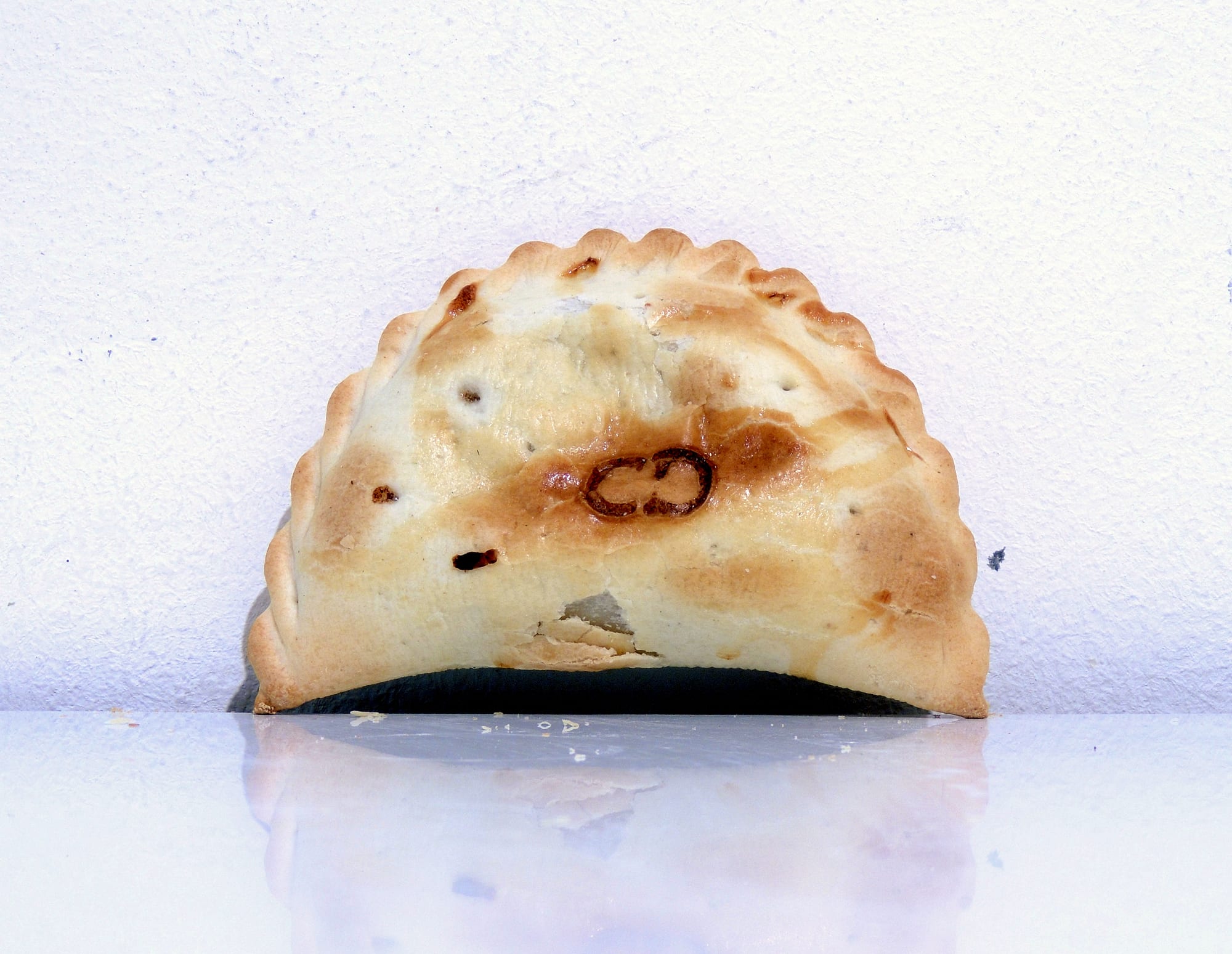 A single crimped, golden-baked empanada seen in profile against a plain background