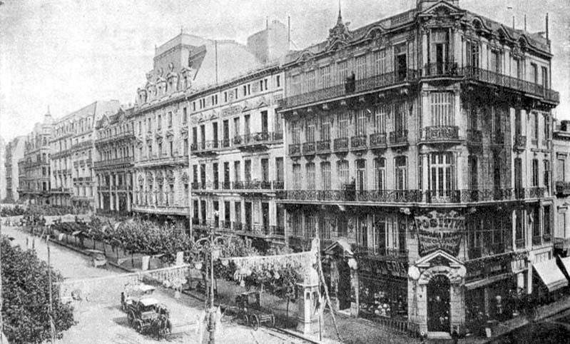 A broad early-1900s avenue lined with ornate European-style buildings, with trams and carriages