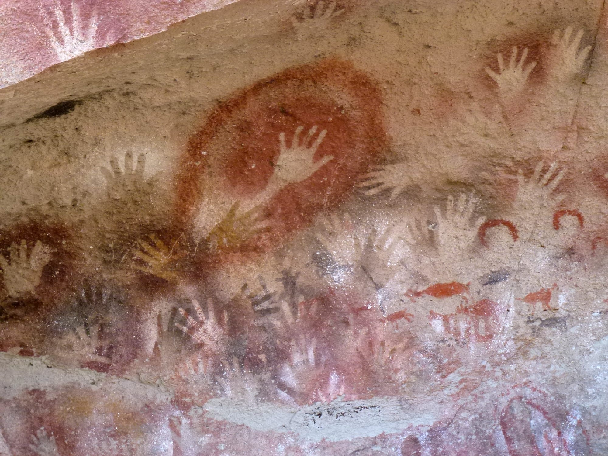 Dozens of stencilled human hands in red and black ochre across a curving rock overhang