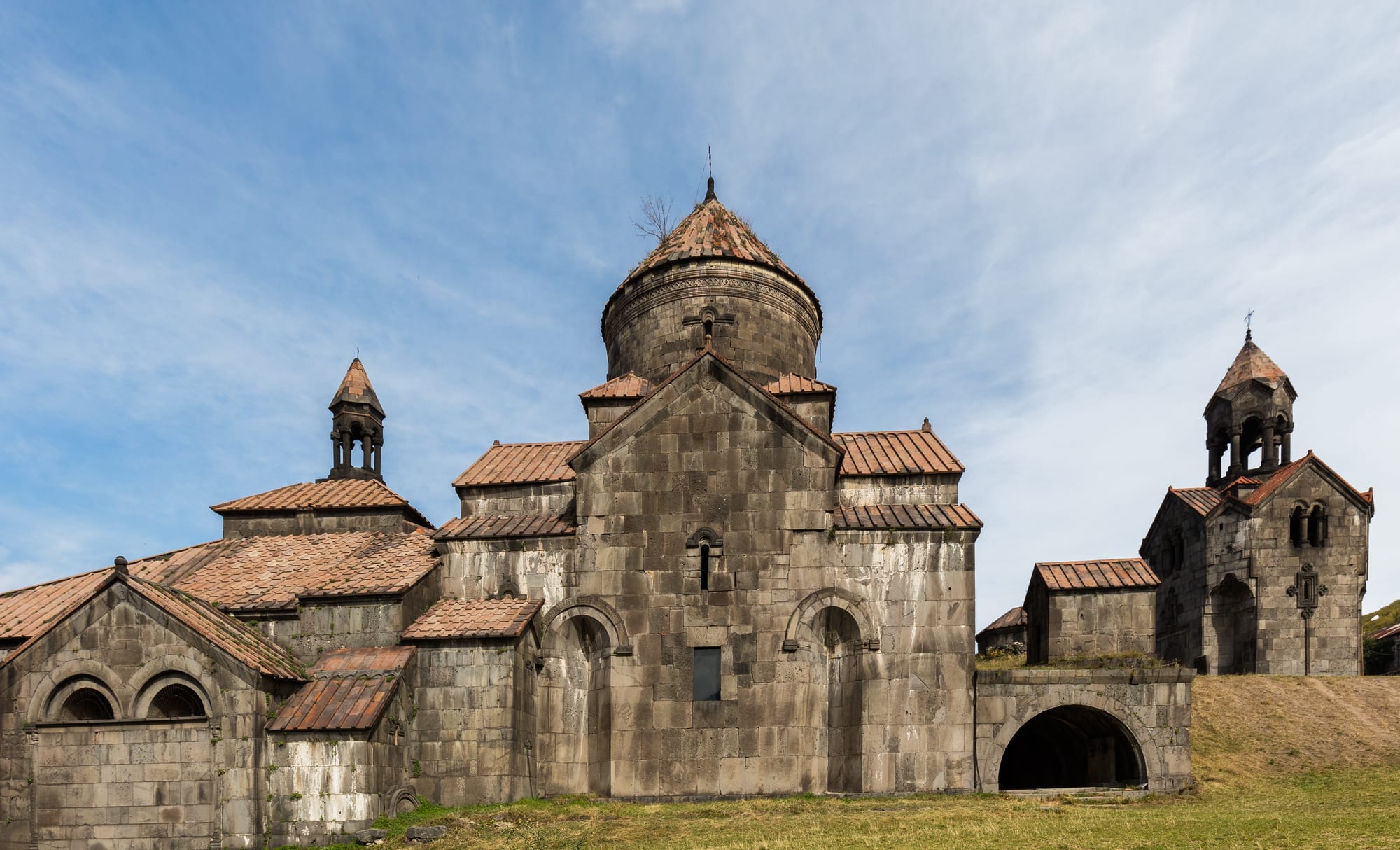 A compact grey monastery with a domed church and bell tower on a green plateau