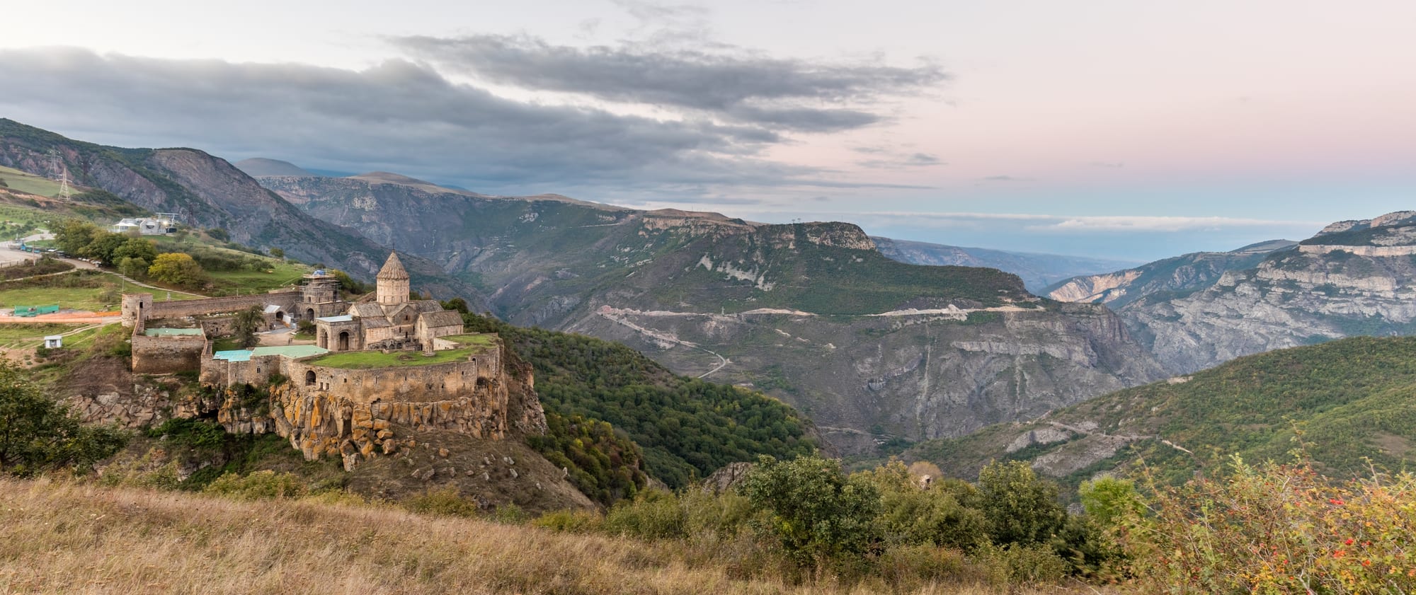 A fortified monastery on a promontory surrounded on three sides by a vast green canyon