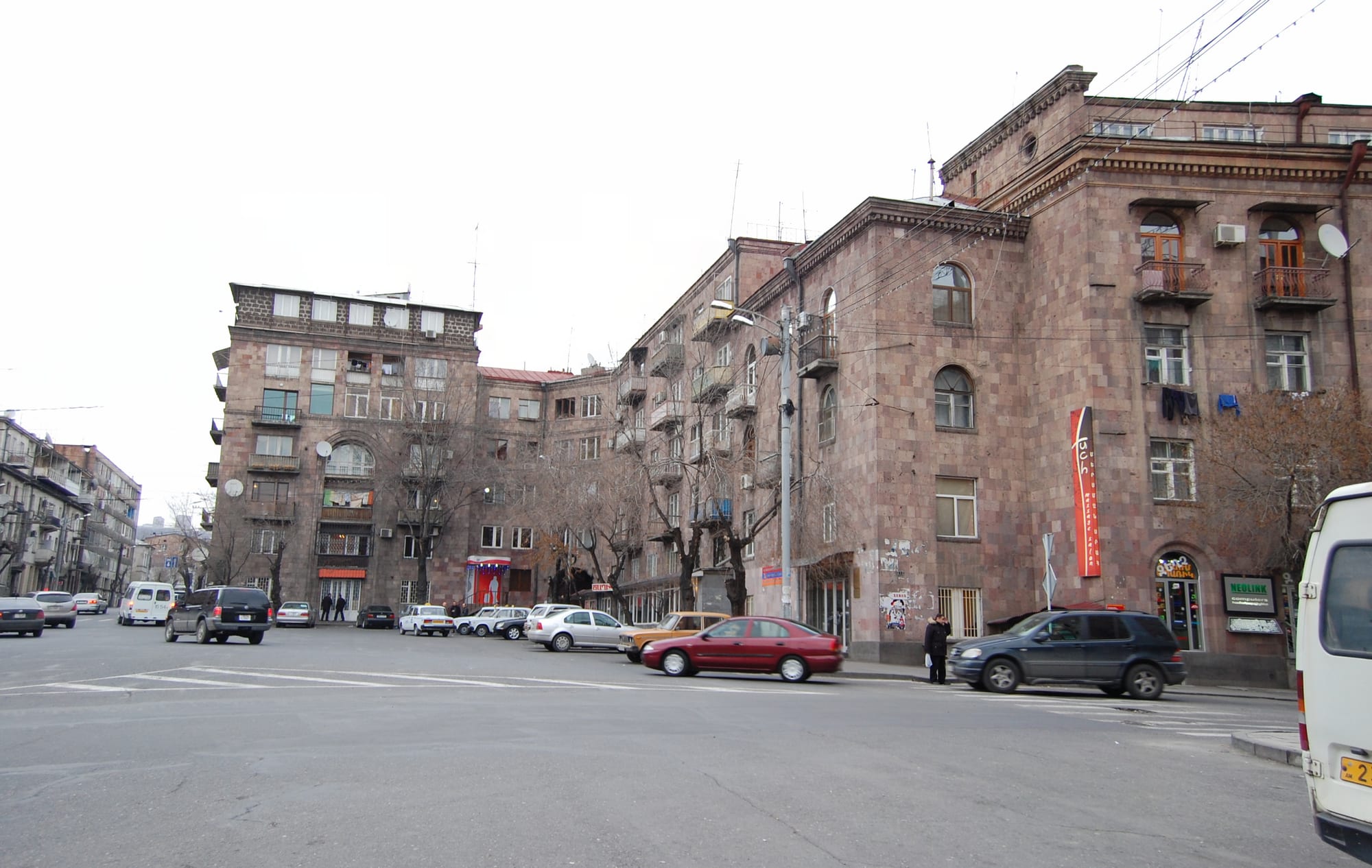 Pink and grey stone apartment blocks several storeys high line a wide street, with parked cars and a few pedestrians below