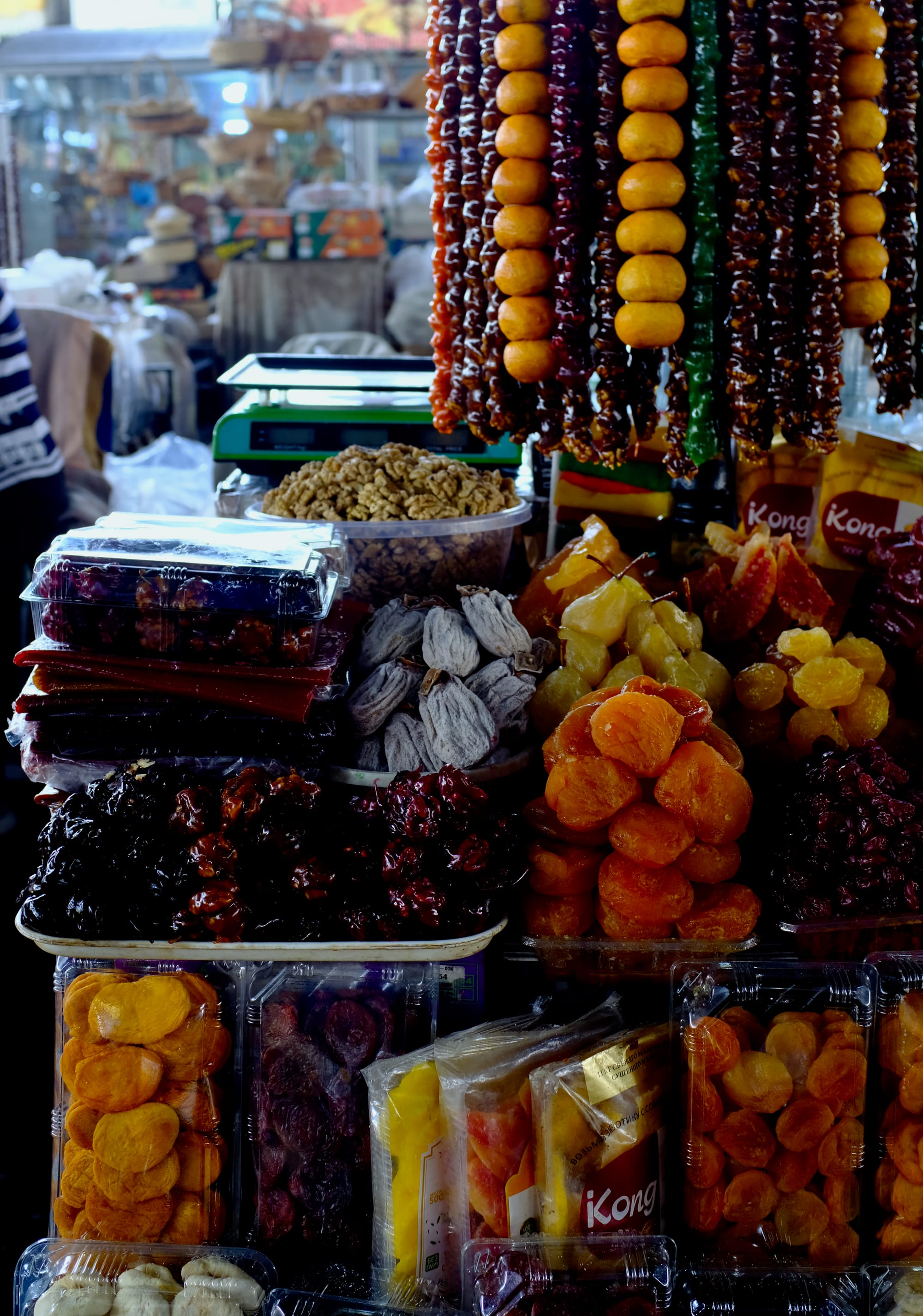 Strings of dried fruit hang above stacked trays of dried apricots, figs, prunes and walnuts at a market stall