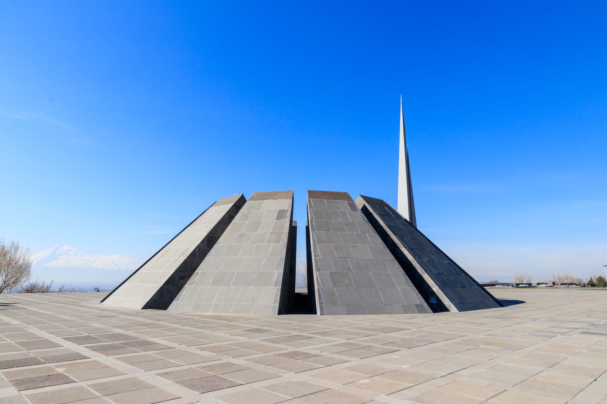 Twelve tall angled stone slabs leaning inward around an eternal flame, with a thin spire alongside