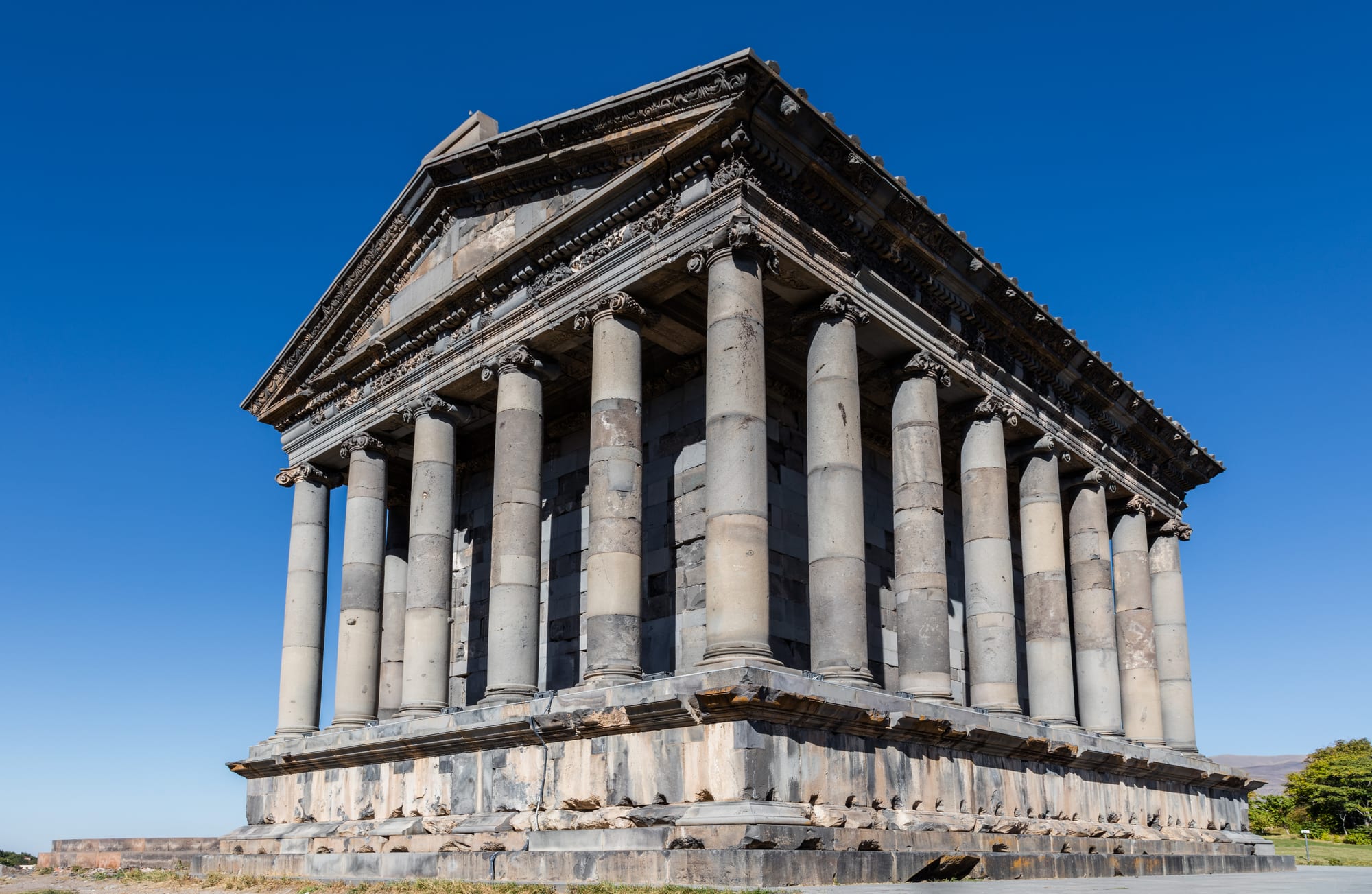 A small Greco-Roman peristyle temple with fluted columns on a green promontory above a gorge