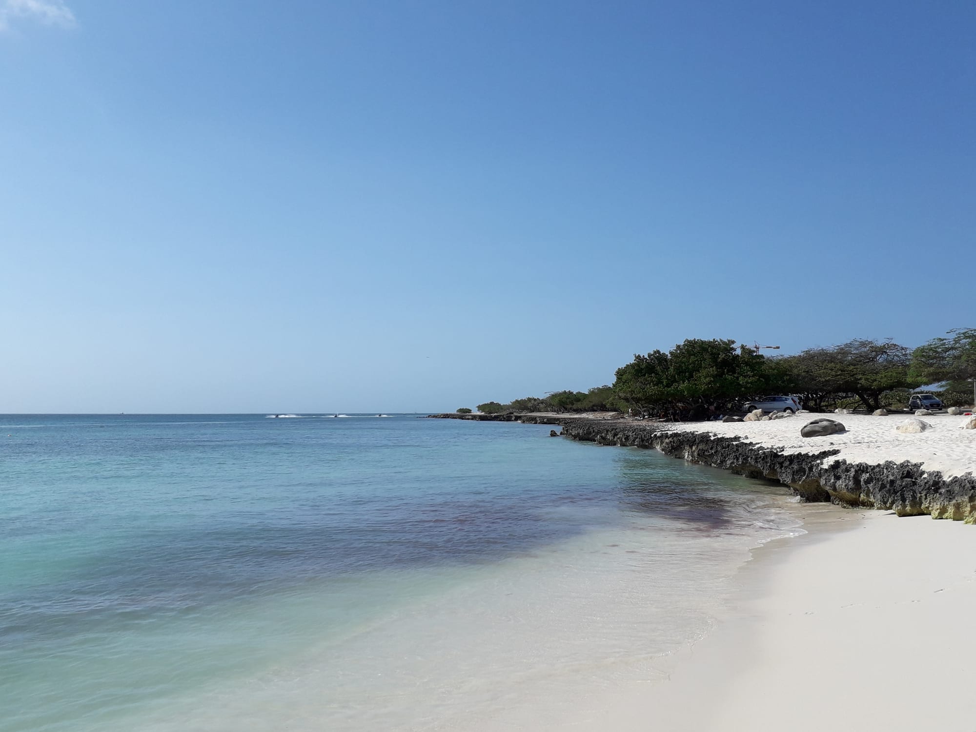 A broad empty stretch of pale sand and gentle turquoise surf under a blue sky