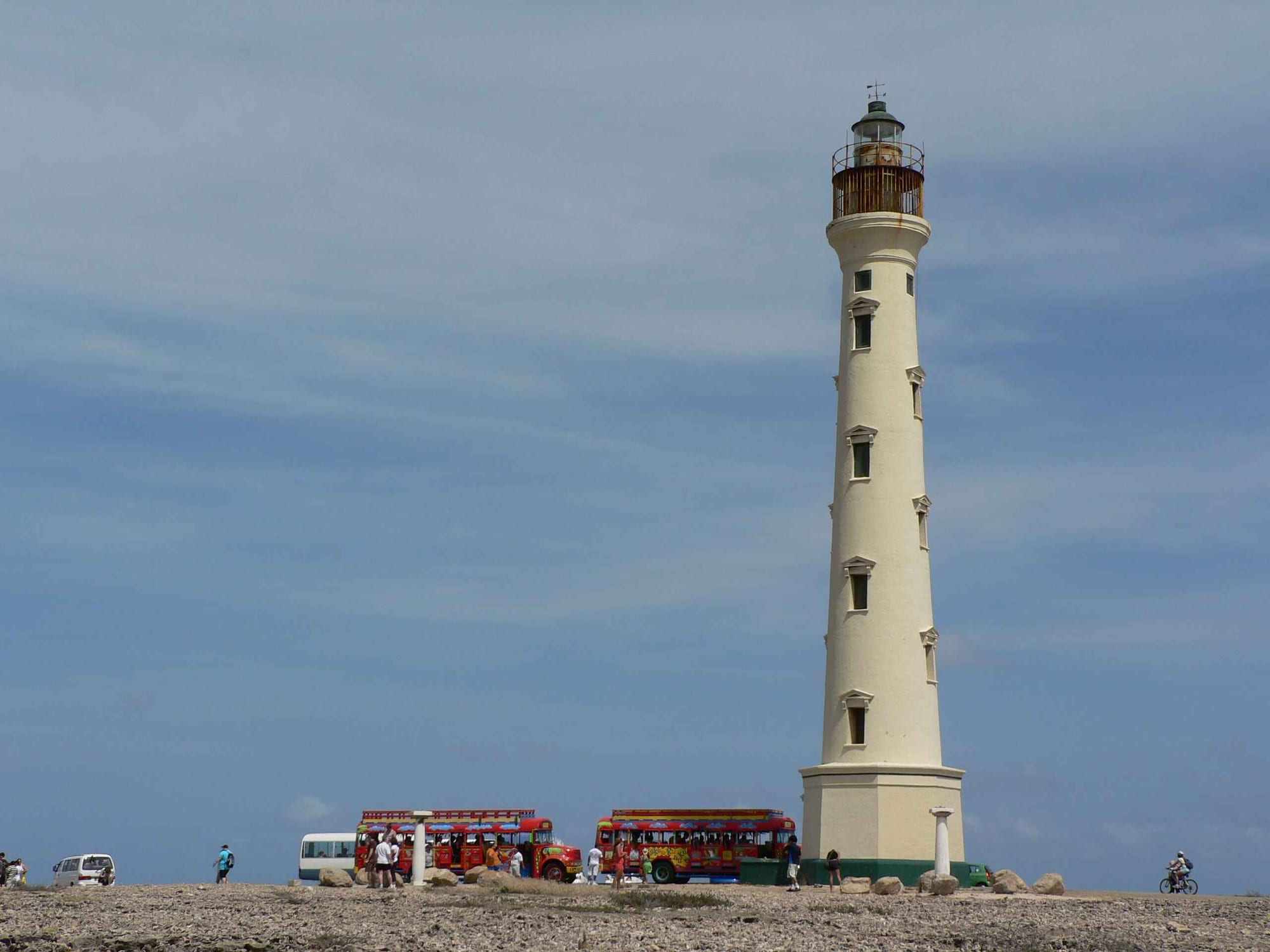 A tall pale stone lighthouse on a low rise of sand dunes and scrub near the sea