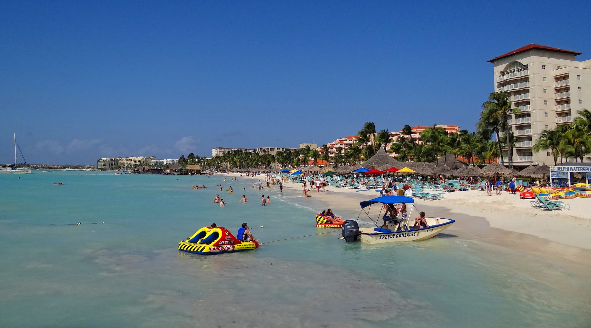 A resort beach lined with tall hotels, palapas and piers, busy with swimmers