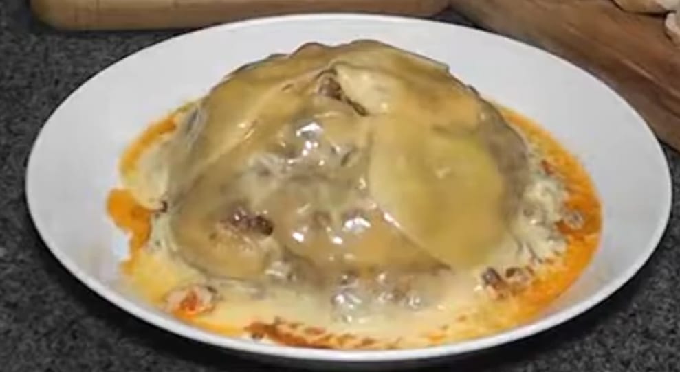 A dome of melted golden cheese over a savoury filling, served on a plate with a light orange sauce pooled around it