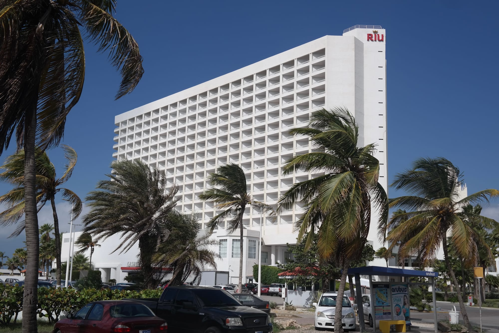 A row of large modern beachfront resort hotels along a wide white-sand beach lined with palm umbrellas