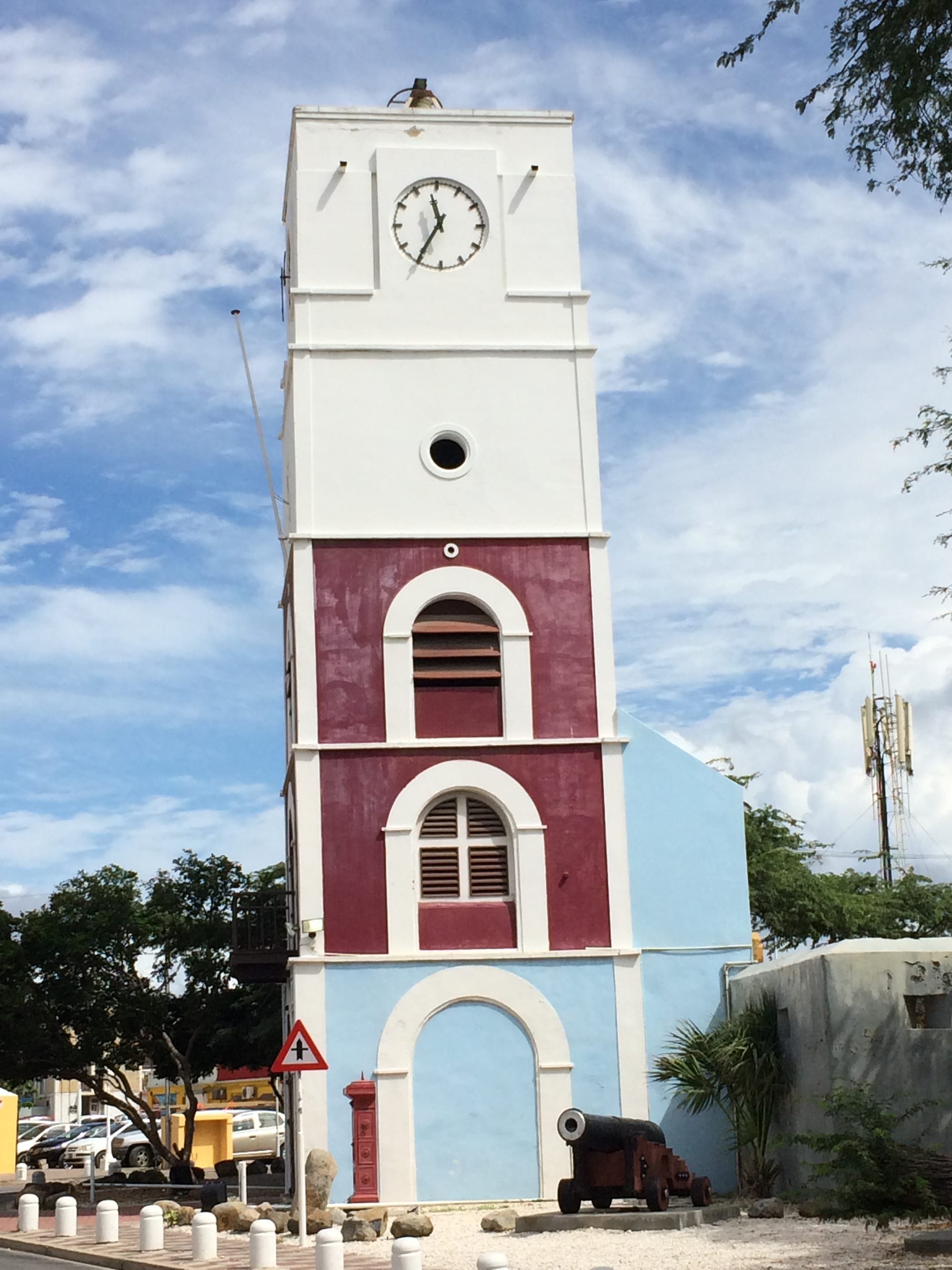 A squat white colonial fort attached to a tall four-sided clock-and-light tower, in a town square