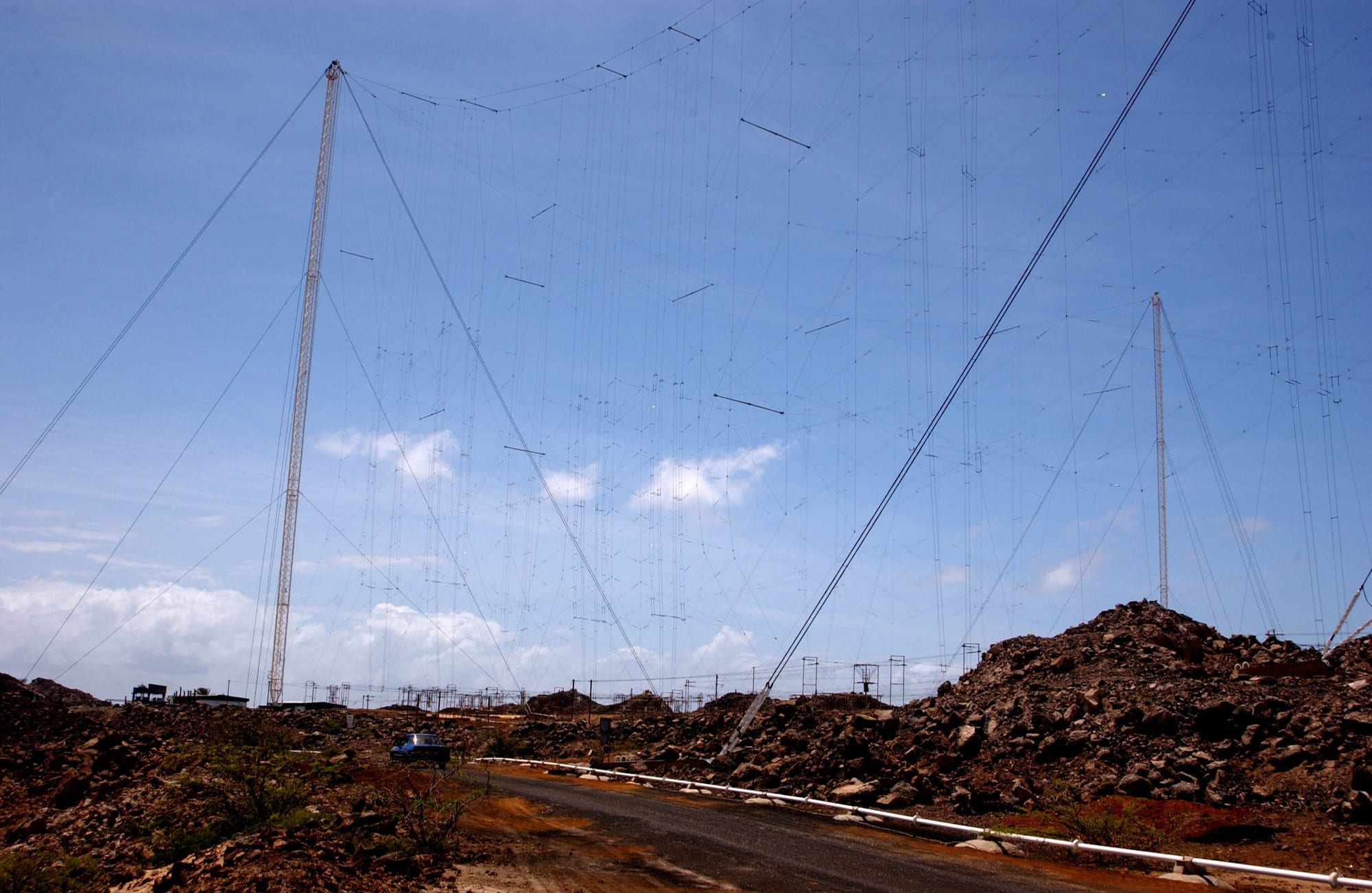 A huge curtain of antenna wires strung between tall steel masts above a road through dark volcanic rubble