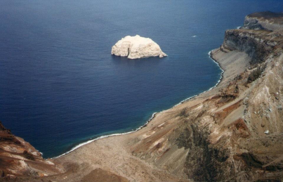 A flat-topped rock island covered in white guano rising sheer from the sea off a lava coast