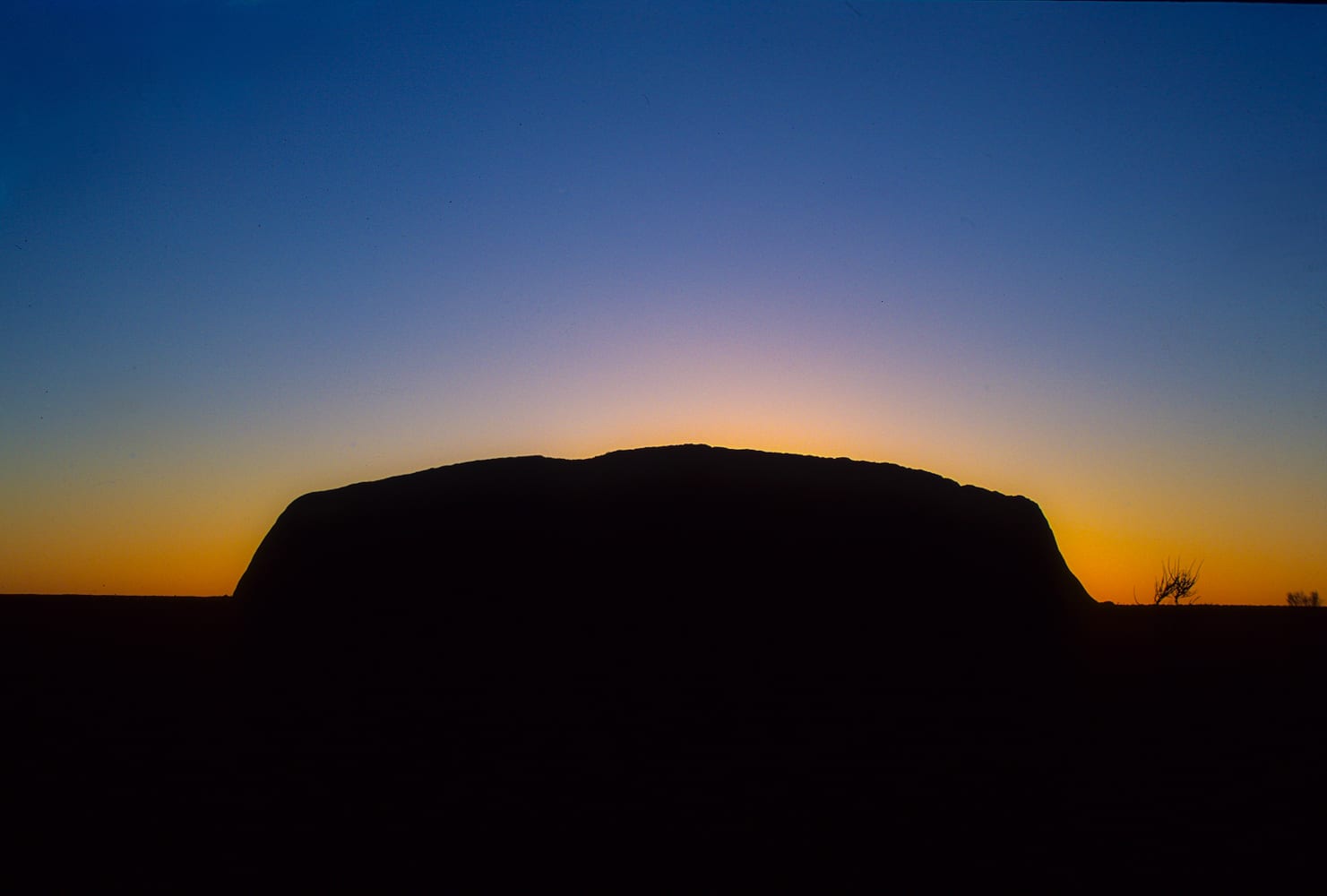 A massive smooth red rock monolith glowing orange against a darkening desert sky