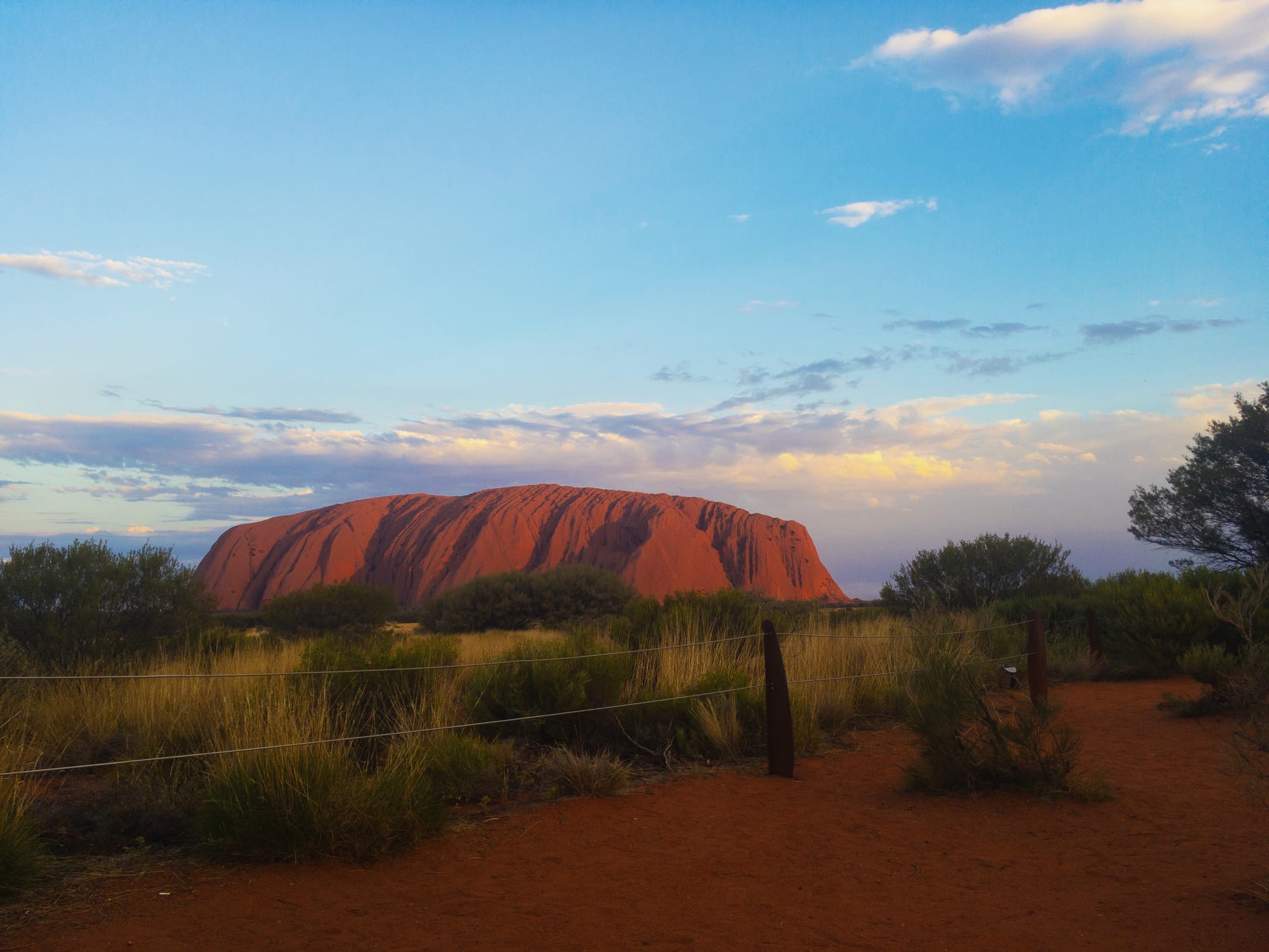 A vast red rock rising from flat desert scrub, its flanks ridged and channelled