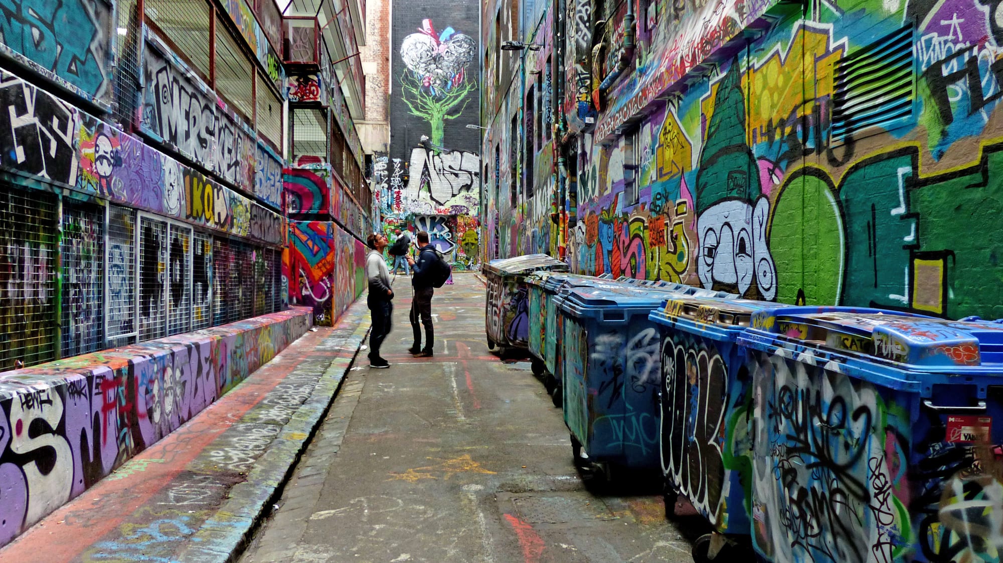 A narrow city lane with every wall surface covered in layered spray-paint art