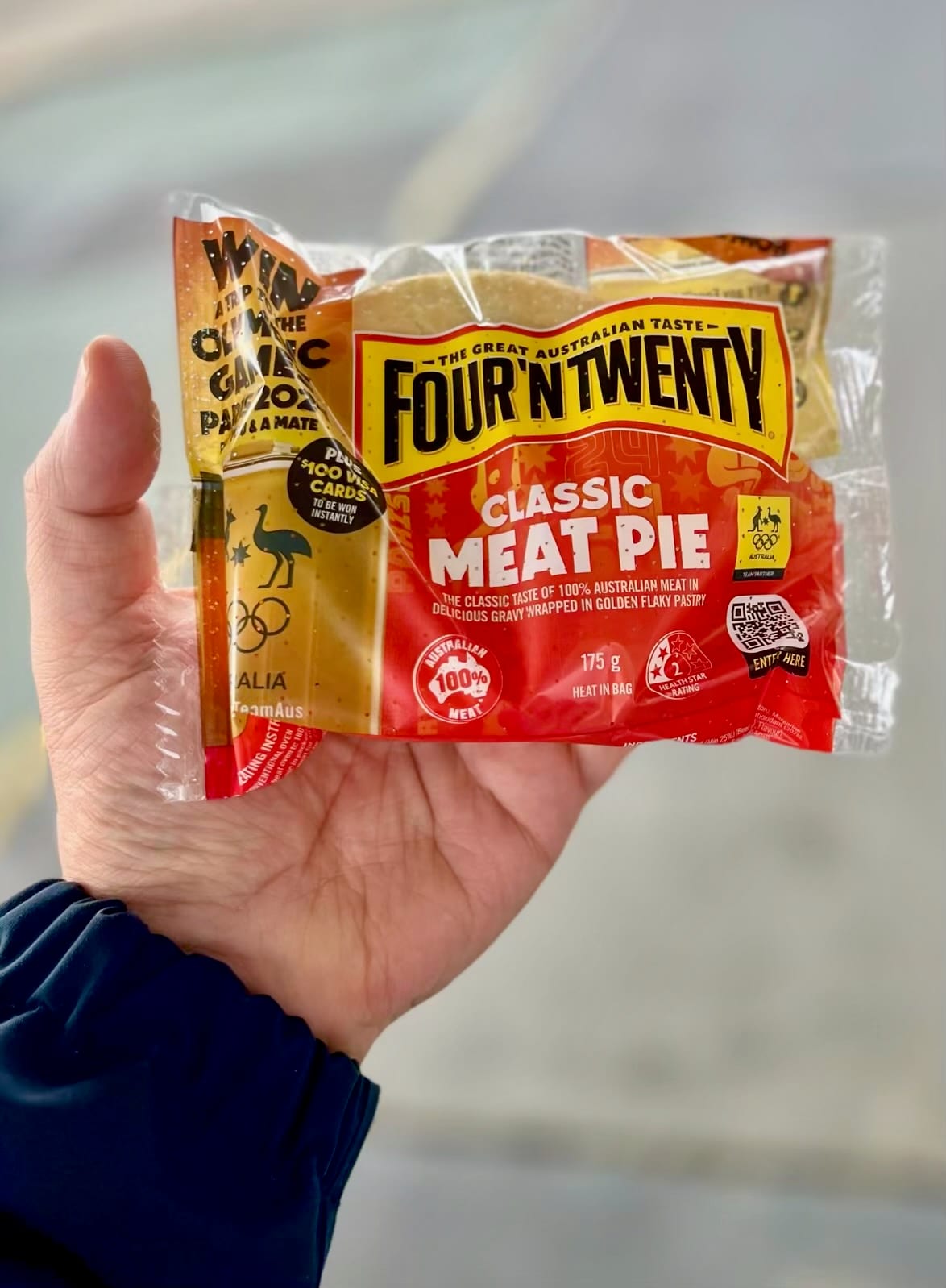 A hand holding a wrapped Four'N Twenty brand classic meat pie