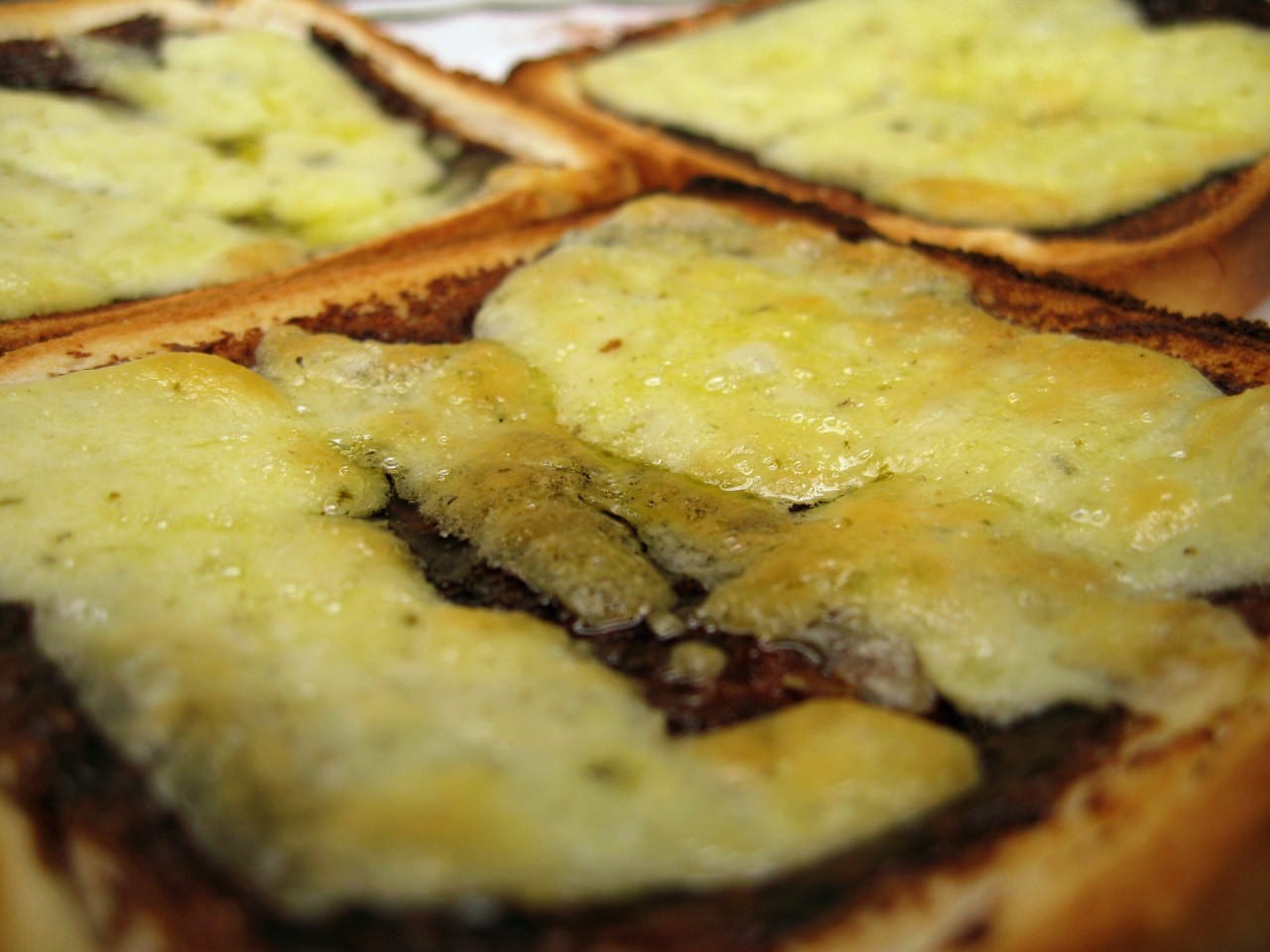 A close-up of melted cheese over toast with a dark spread visible underneath