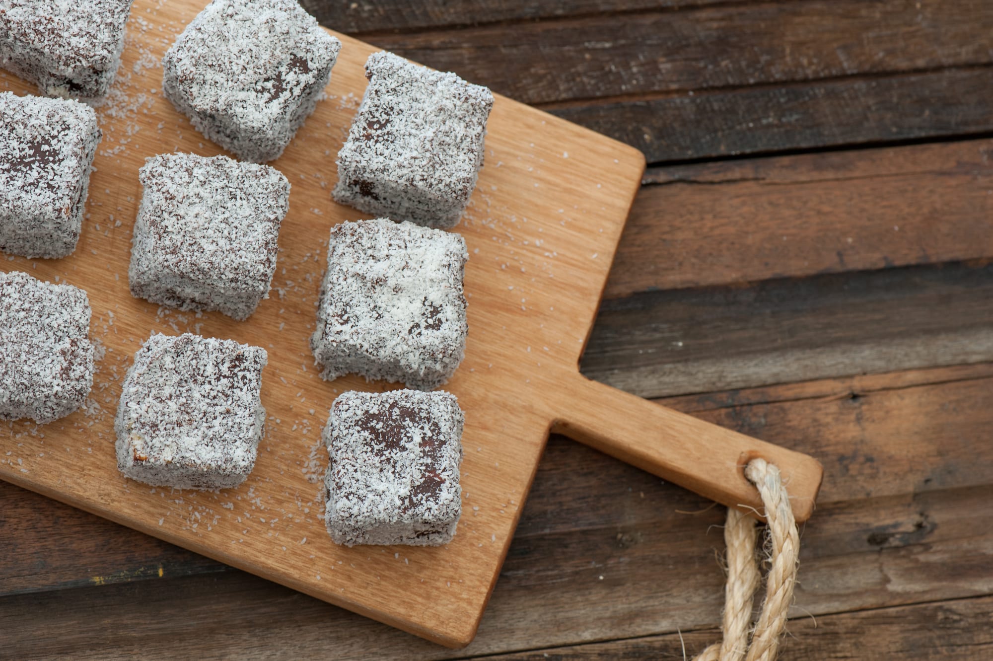 Squares of sponge cake coated in chocolate and rolled in coconut, arranged on a wooden board