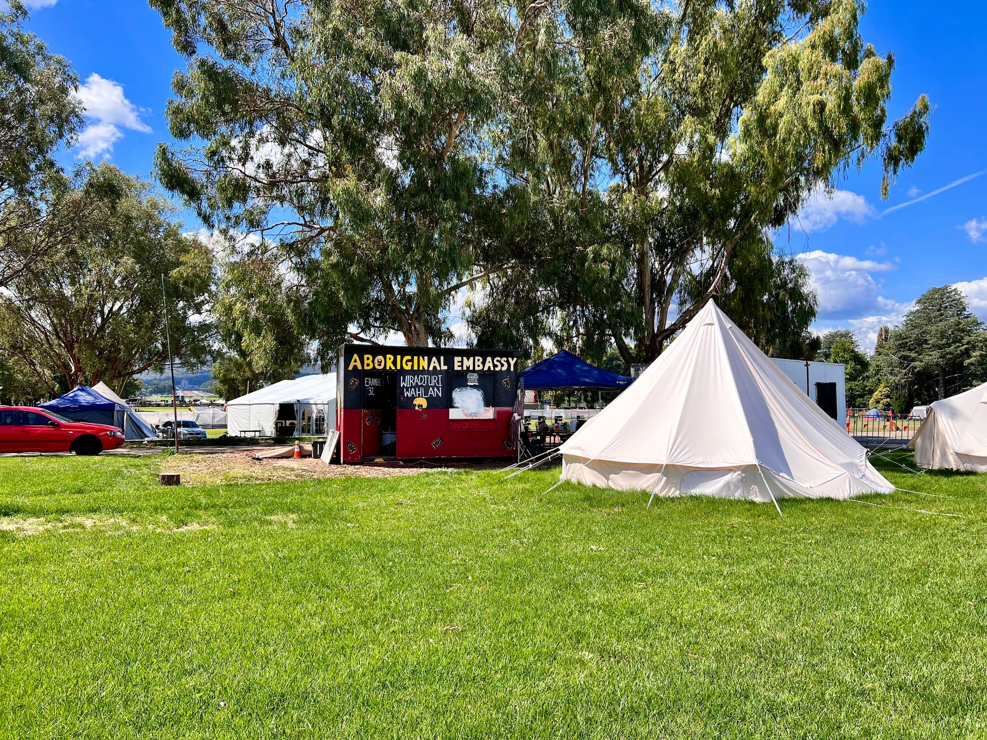 A cluster of tents, painted signs and Aboriginal flags on a lawn in front of a white colonnaded building