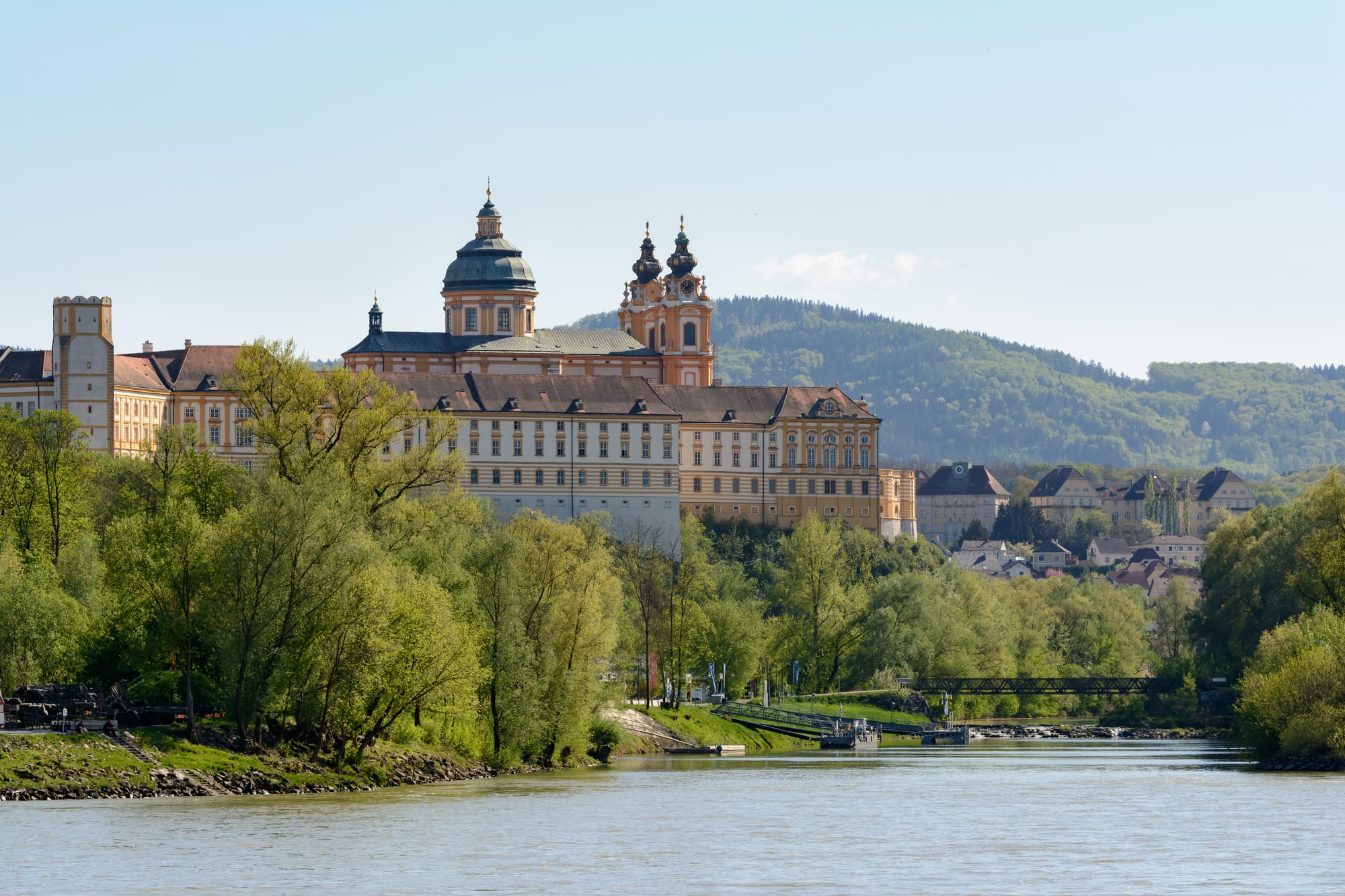An enormous yellow baroque abbey on a rock above a river, with twin towers and a dome