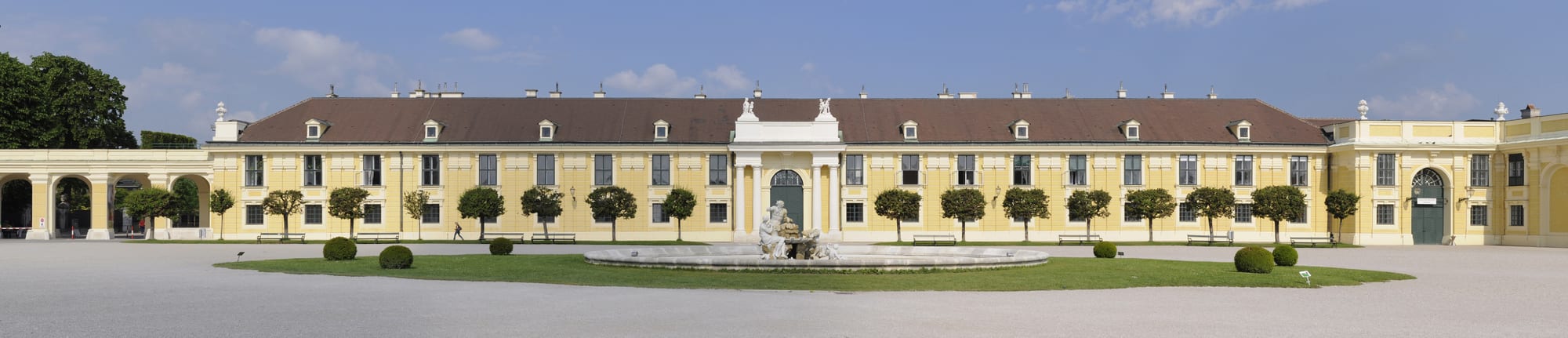 A long yellow baroque palace behind formal parterre gardens