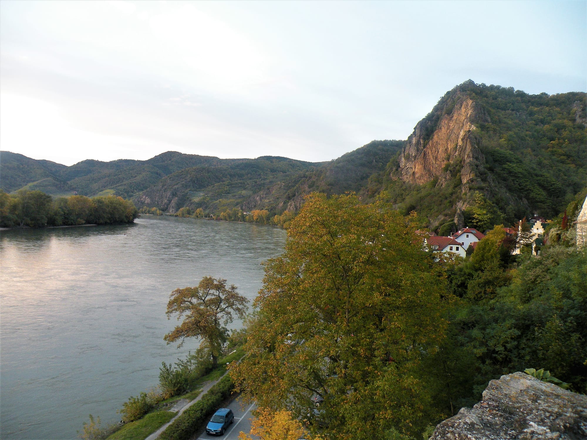 A blue baroque church tower in a small town on a river, terraced vineyards and a ruined castle above