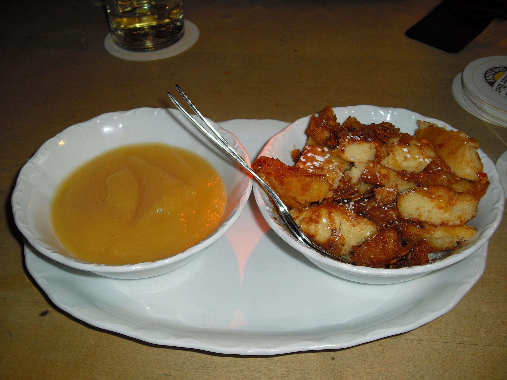 Torn, caramelised pancake pieces dusted with powdered sugar in a bowl, next to a bowl of pale apple sauce