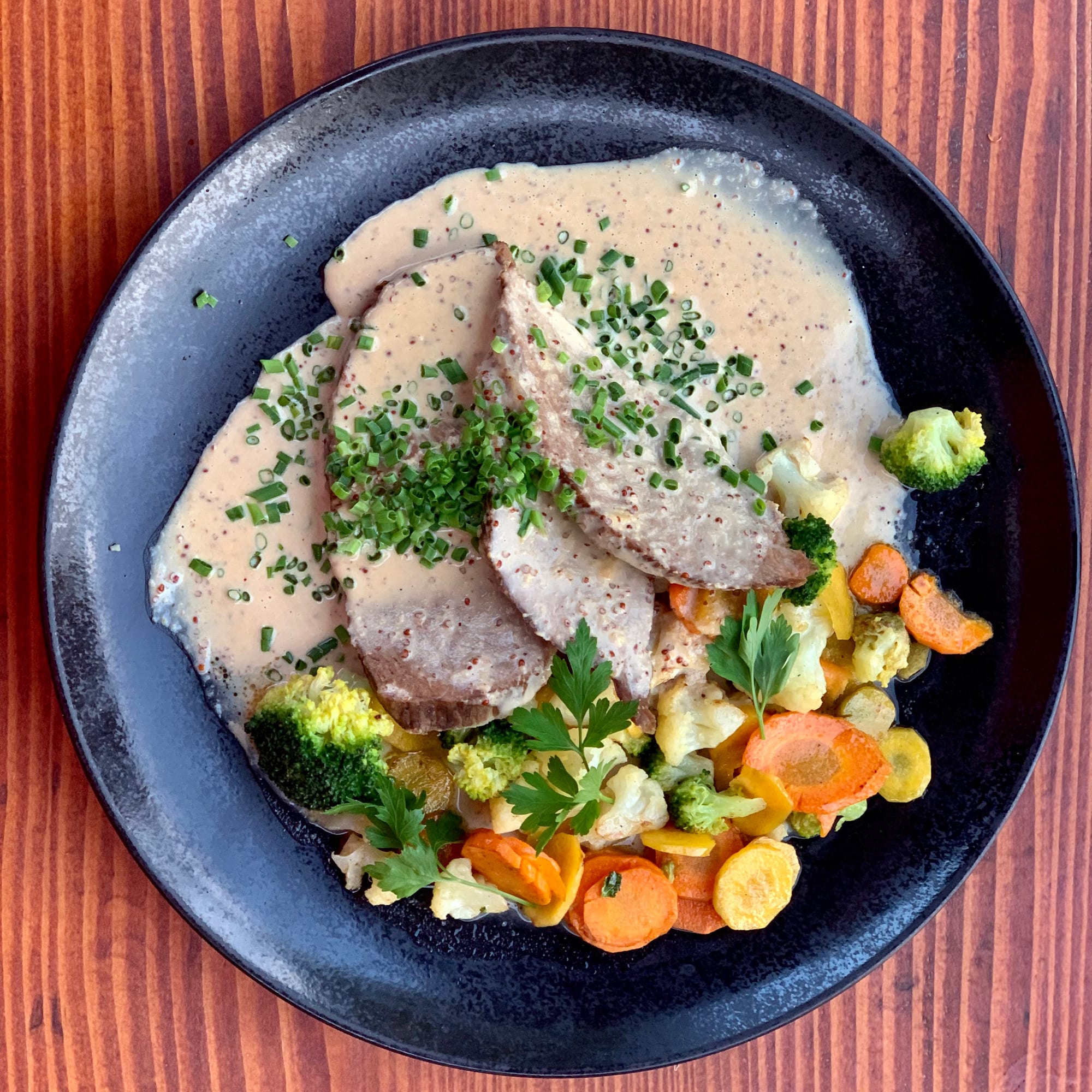 Sliced boiled beef topped with a creamy chive sauce, served with a mix of steamed carrots, broccoli and cauliflower