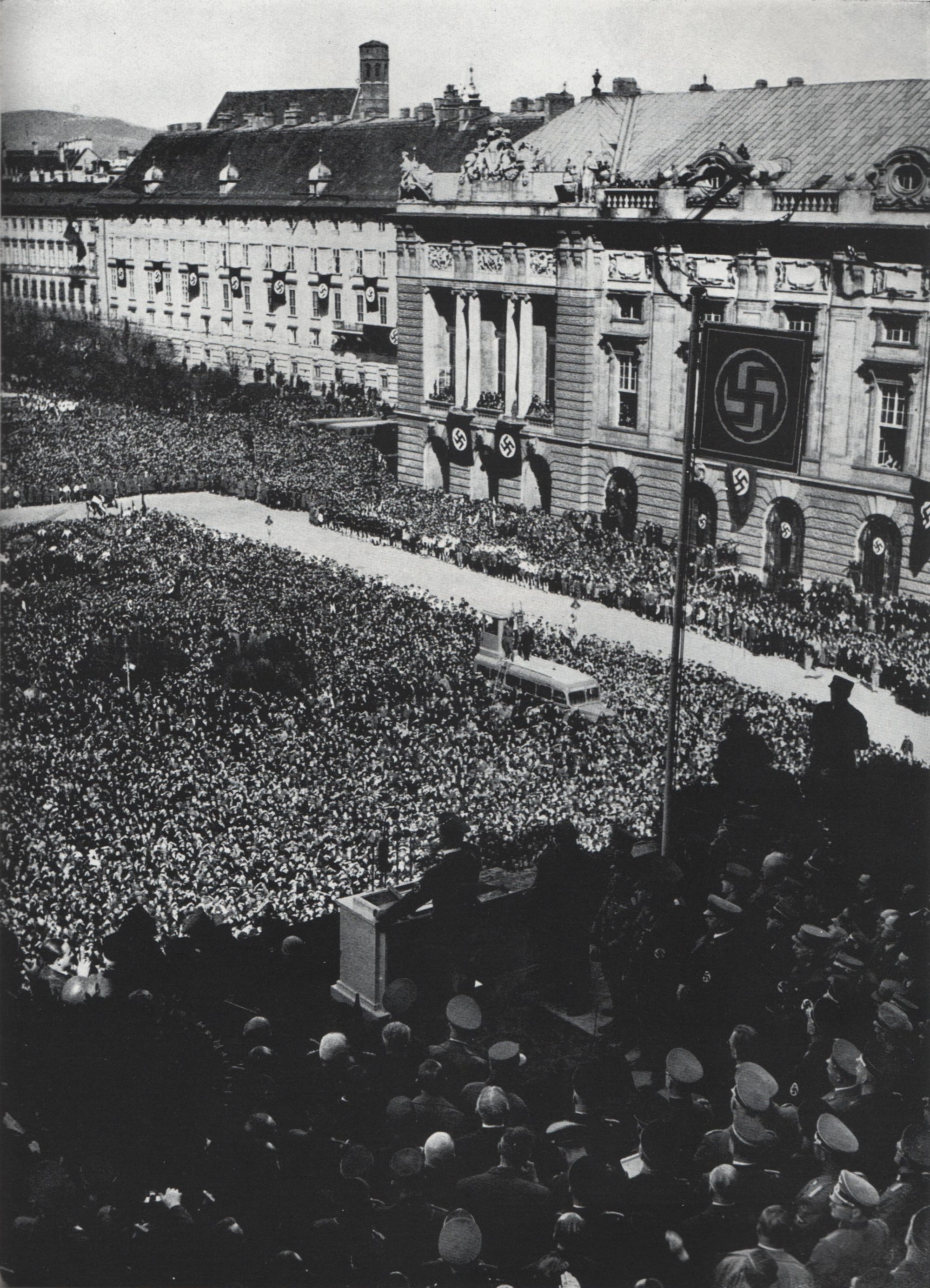 An enormous 1938 crowd packing a Vienna square in front of a palace, arms raised