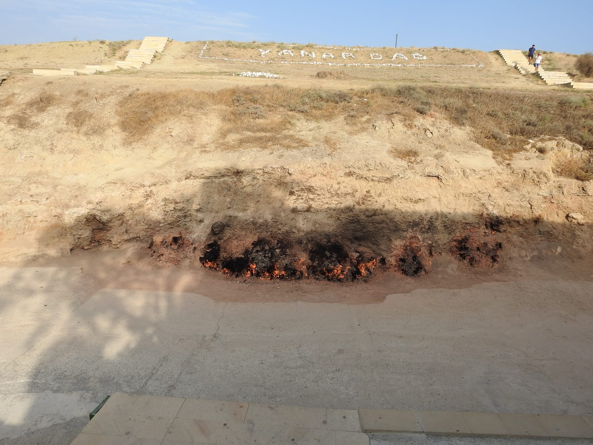 A wall of flames burning along the base of a low bare hillside
