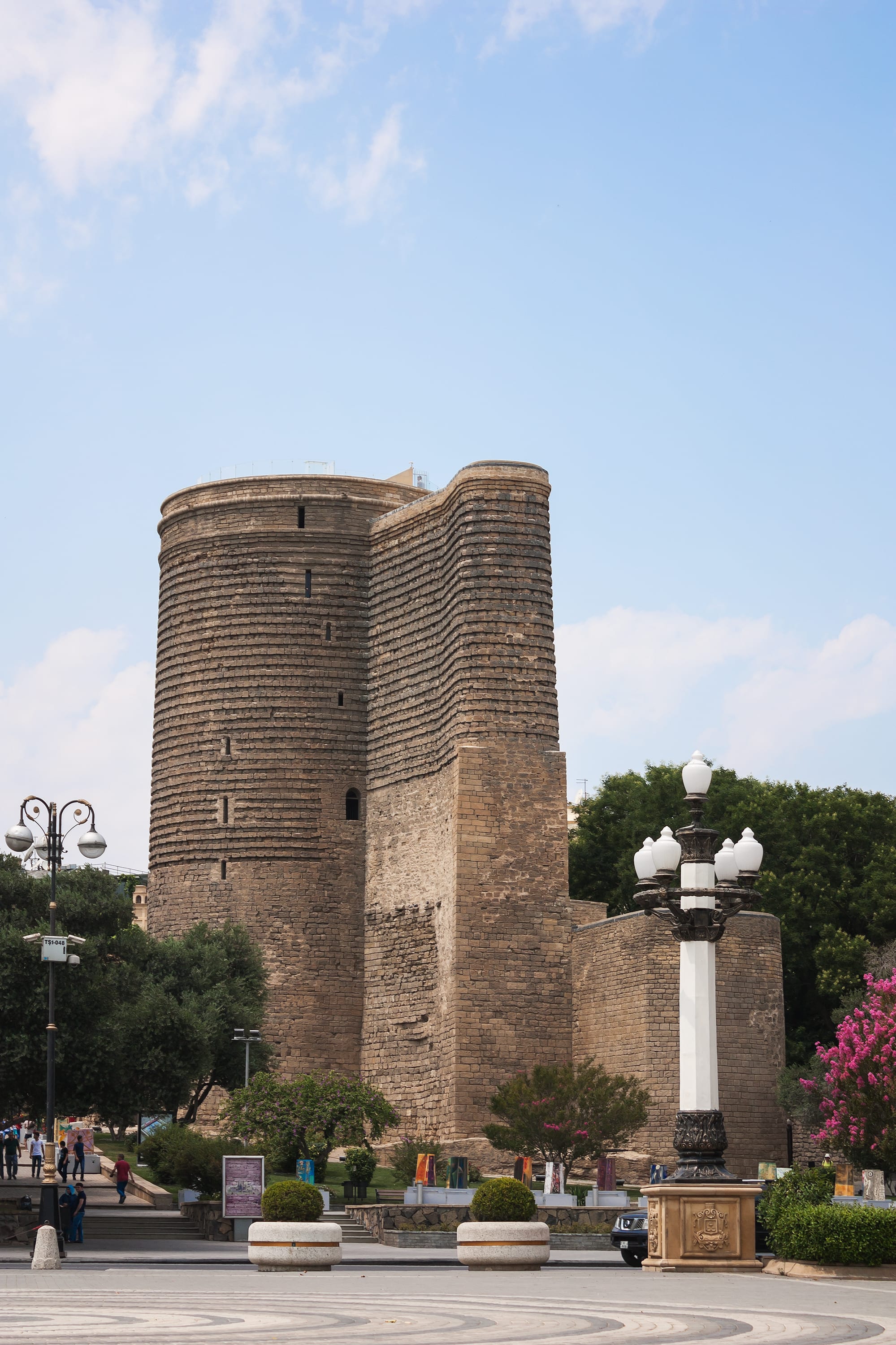 A tall, tapering cylindrical stone tower with a projecting buttress, in an old-town square
