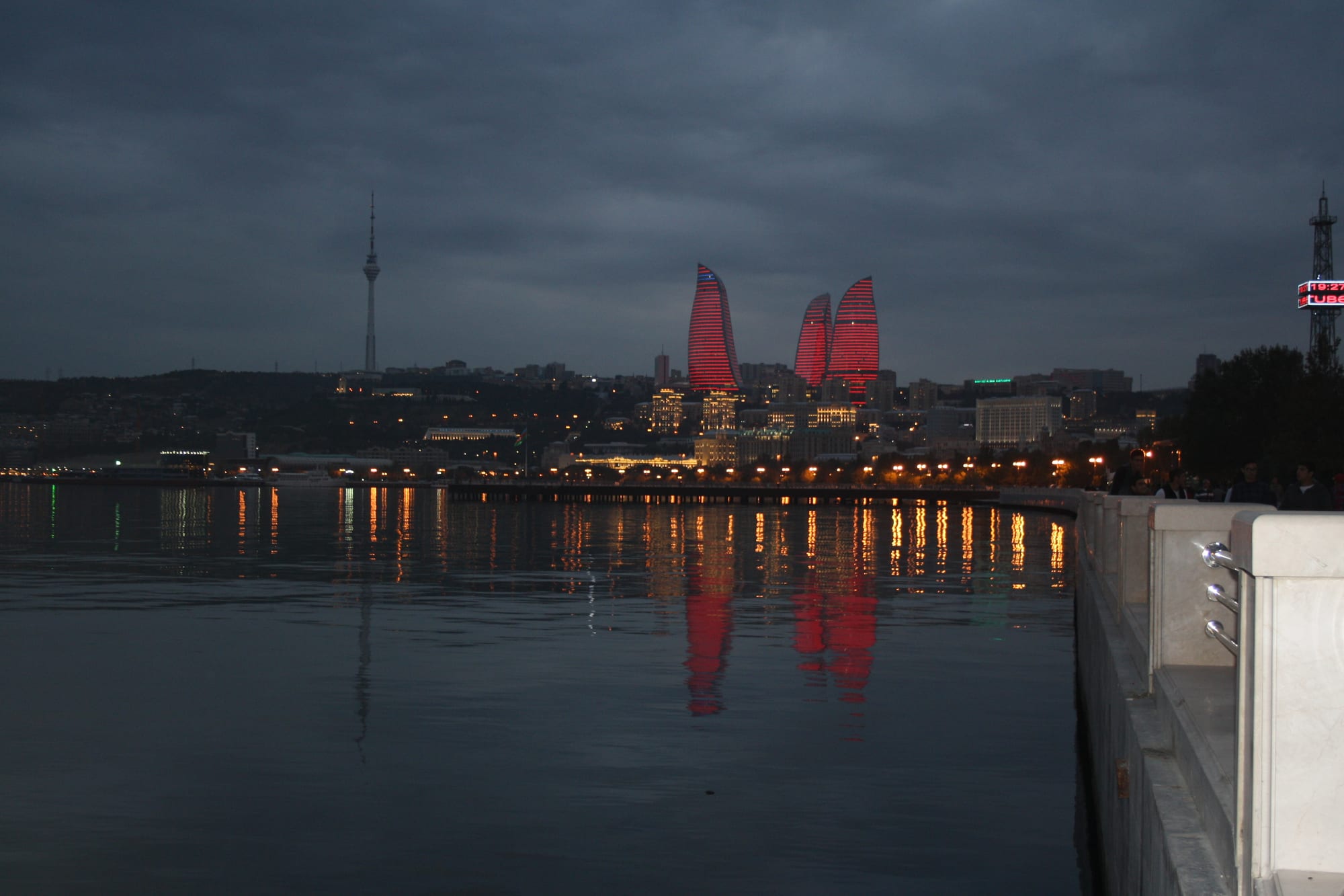 Three curved glass skyscrapers shaped like flames rising above an older city and a bay