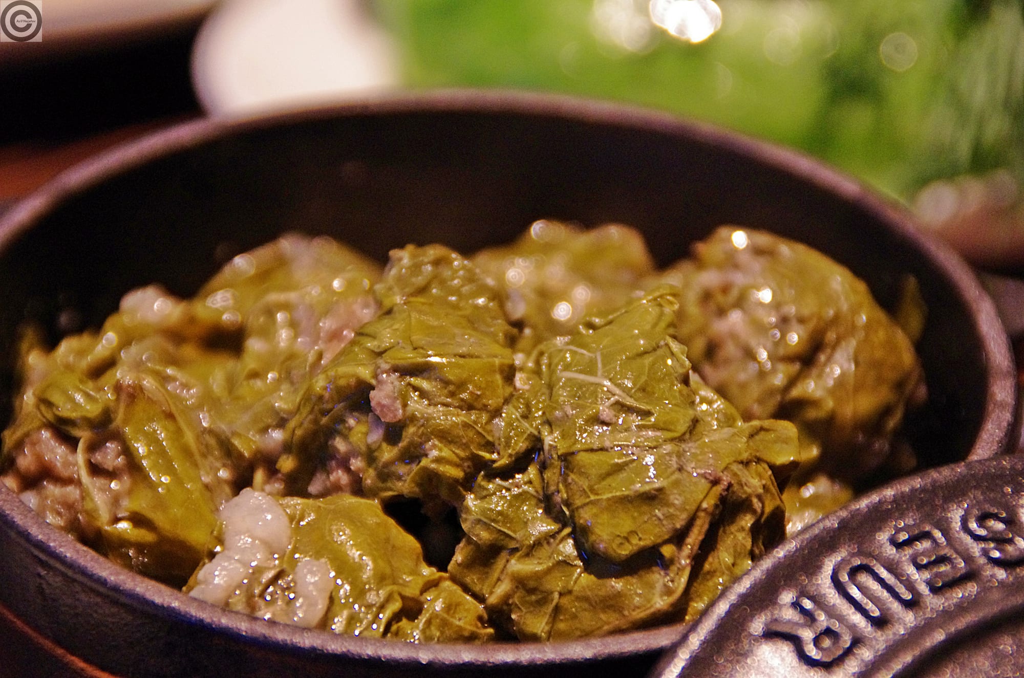 A small dark pot holding several grape-leaf-wrapped rolls with a visible rice and meat filling