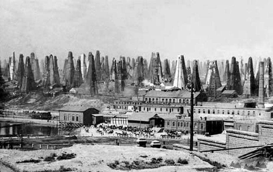 An old photograph of oil wells and industrial buildings with a pipeline running through