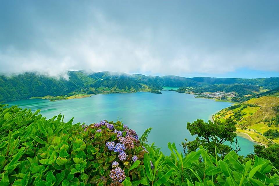A caldera rim path looking down on two lakes and a small village on the isthmus between them