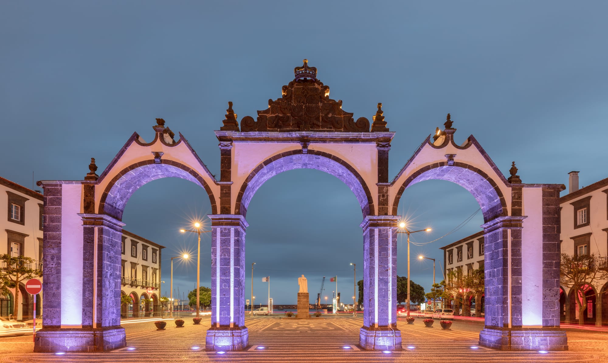Three white stone archways standing on a waterfront plaza in front of black-and-white churches