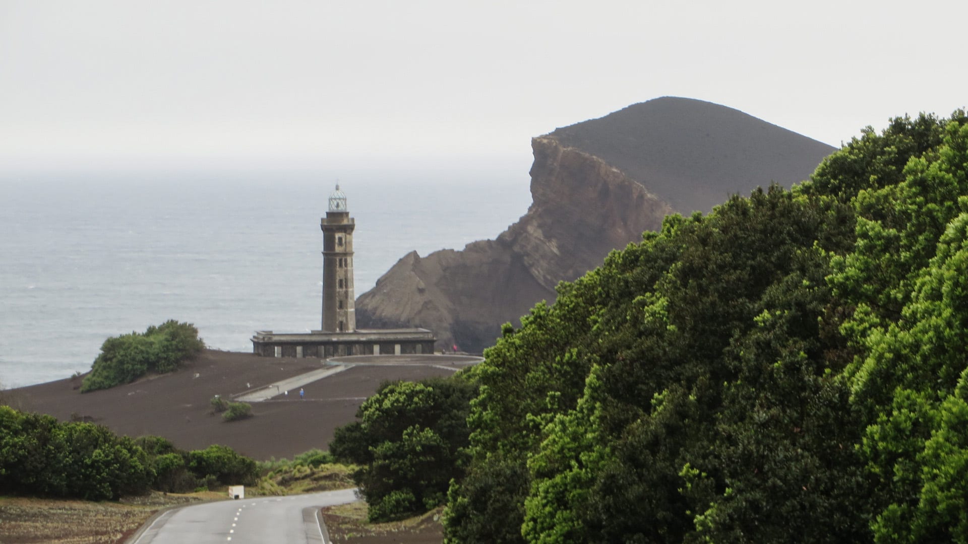 A half-buried lighthouse on a grey ash plain running out to the sea