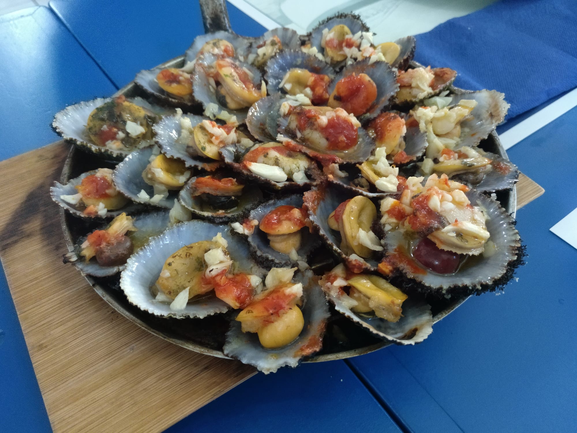 A large platter piled with grilled limpets in their shells, topped with garlic and tomato