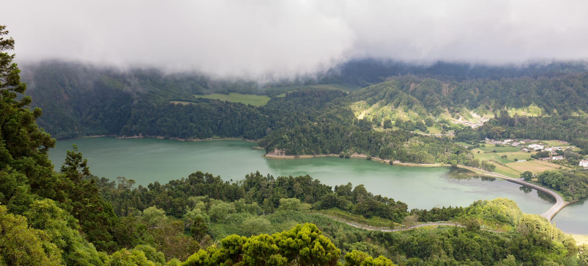 Two crater lakes, one blue and one green, filling a broad volcanic caldera ringed by forested slopes