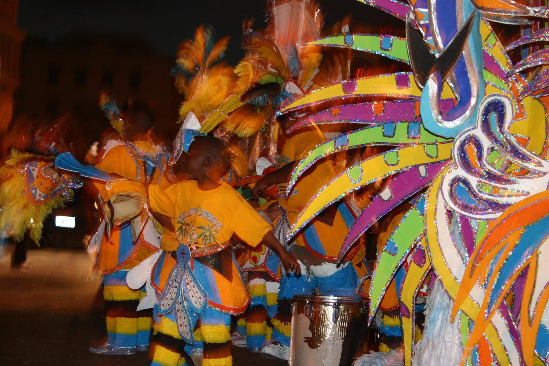 Dancers in huge feathered and crepe-paper costumes parading down a street