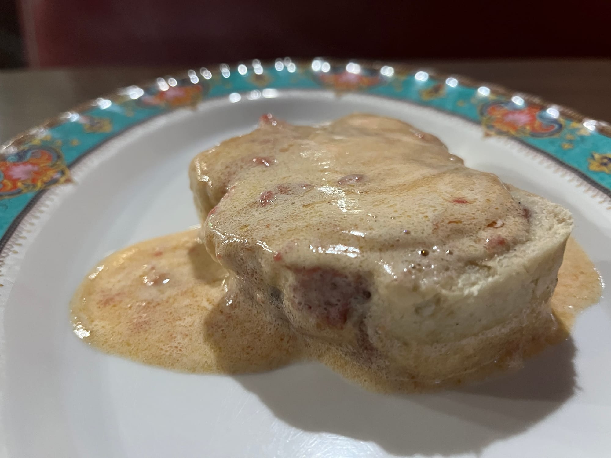 A slice of pale, rolled pastry with pink guava filling swirled through it, covered in a glossy sauce