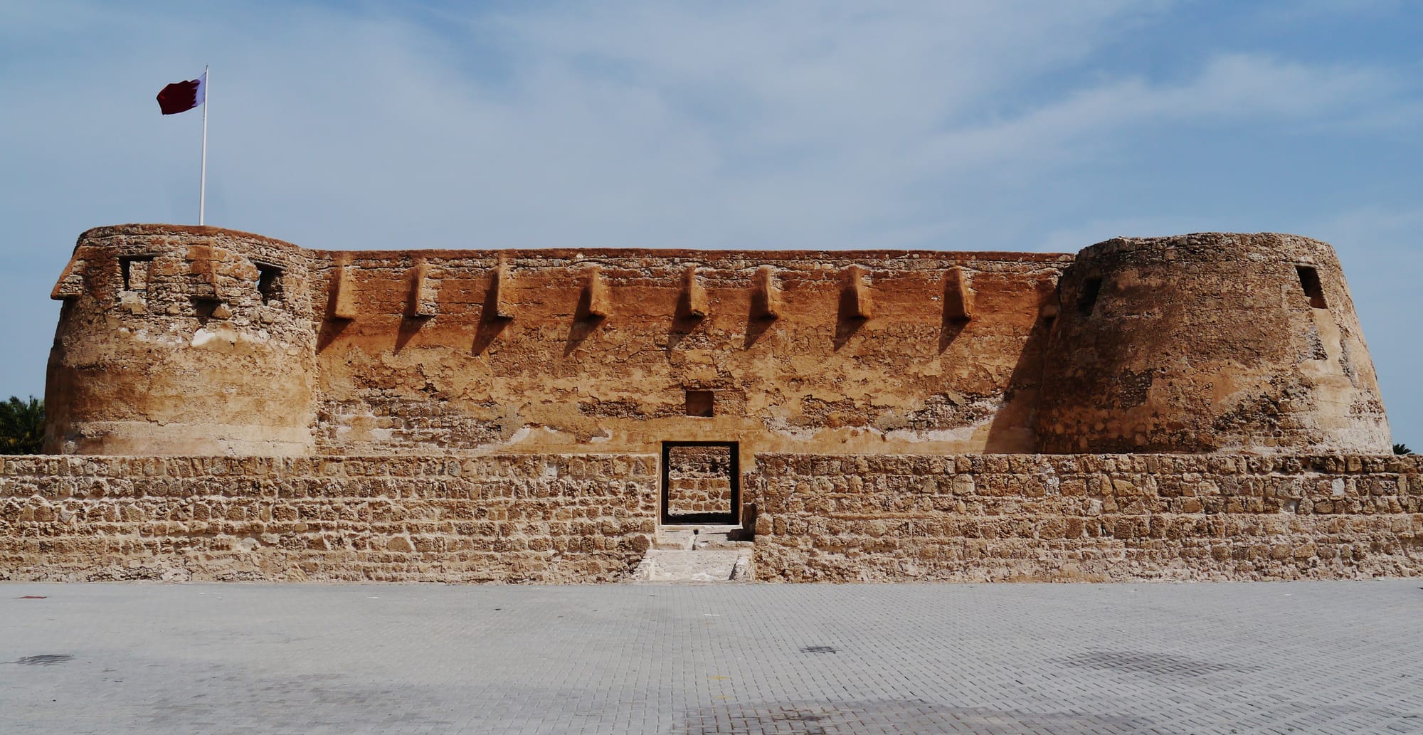A compact white fort with rounded corner towers and a dry moat, palms behind