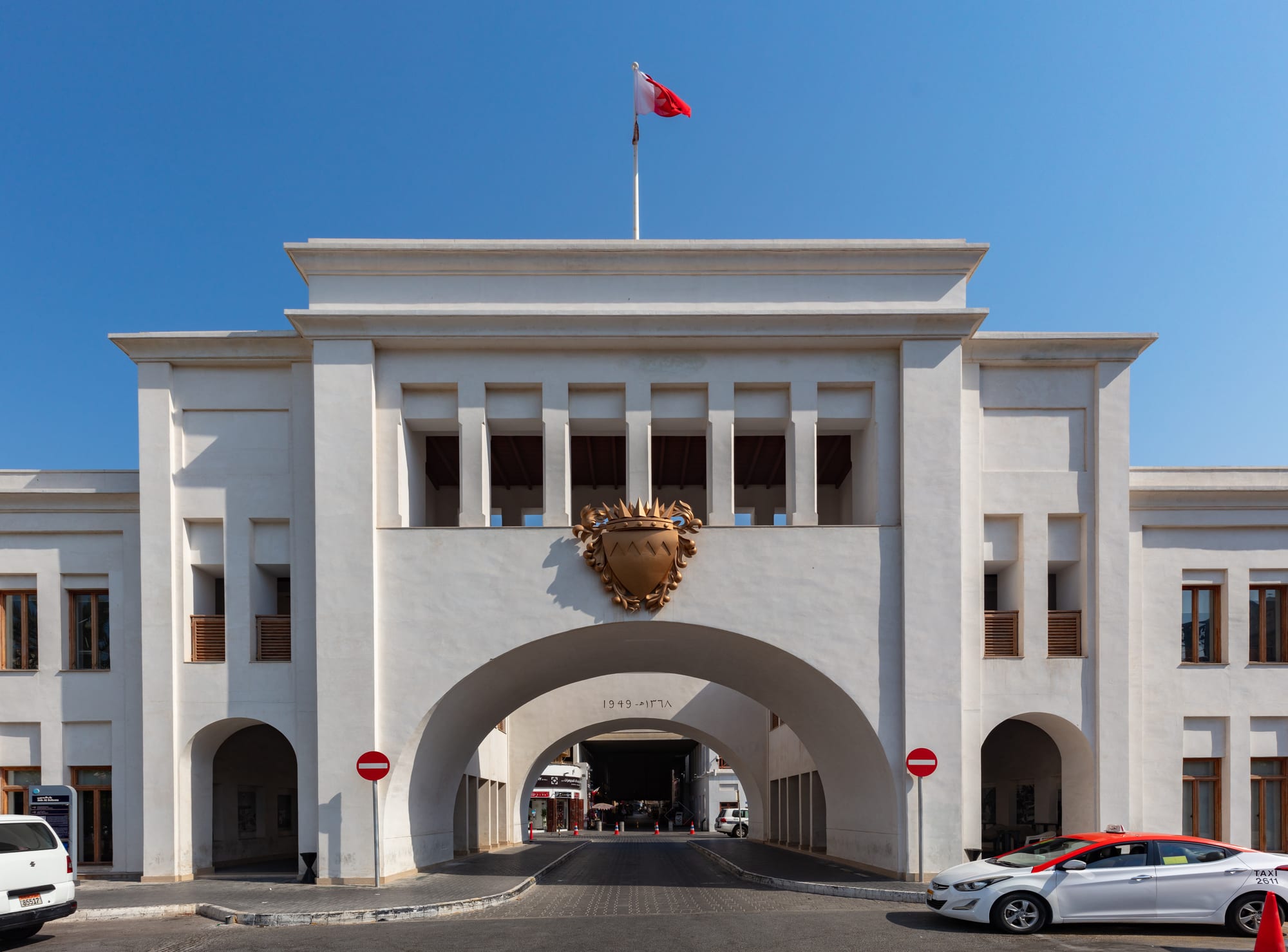 A grand cream-coloured arched gateway building at the entrance to a market street, cars passing beneath